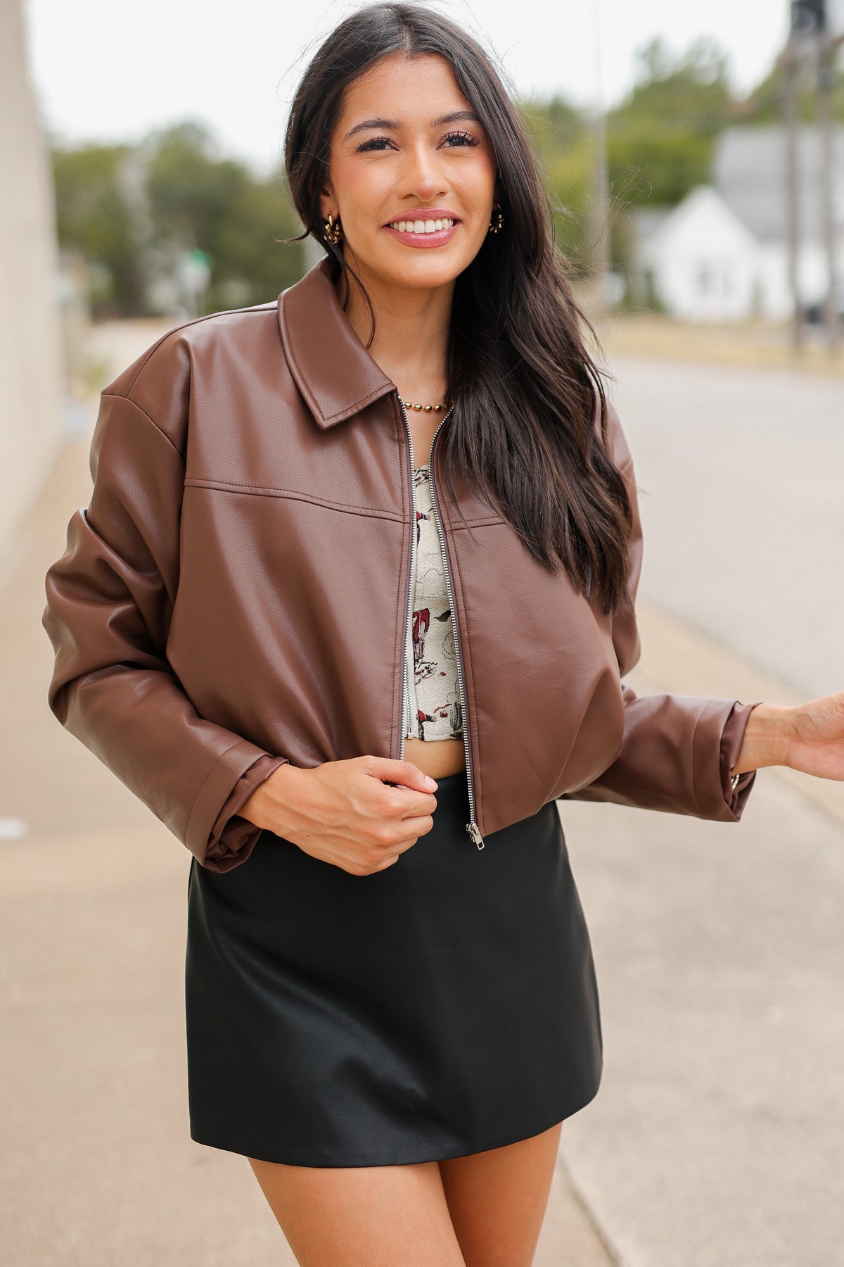 Model wearing the Riverton Cropped Faux Leather Jacket in Chocolate with the Briar black mini skirt and Amaya red western boots, featuring a relaxed silhouette and zip-front design. Southern House Clothing
