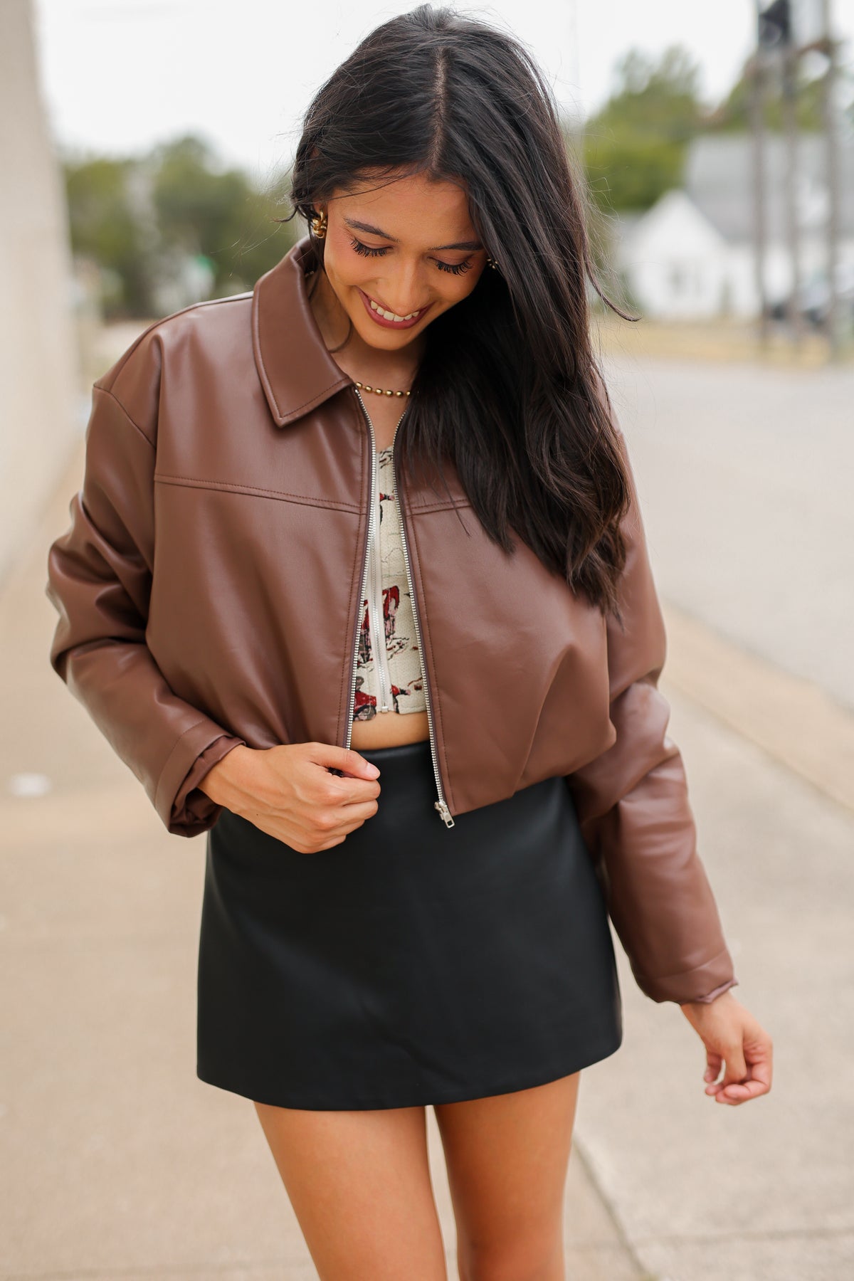 Model wearing the Riverton Cropped Faux Leather Jacket in Chocolate with the Briar black mini skirt and Amaya red western boots, featuring a relaxed silhouette and zip-front design. Southern House Clothing