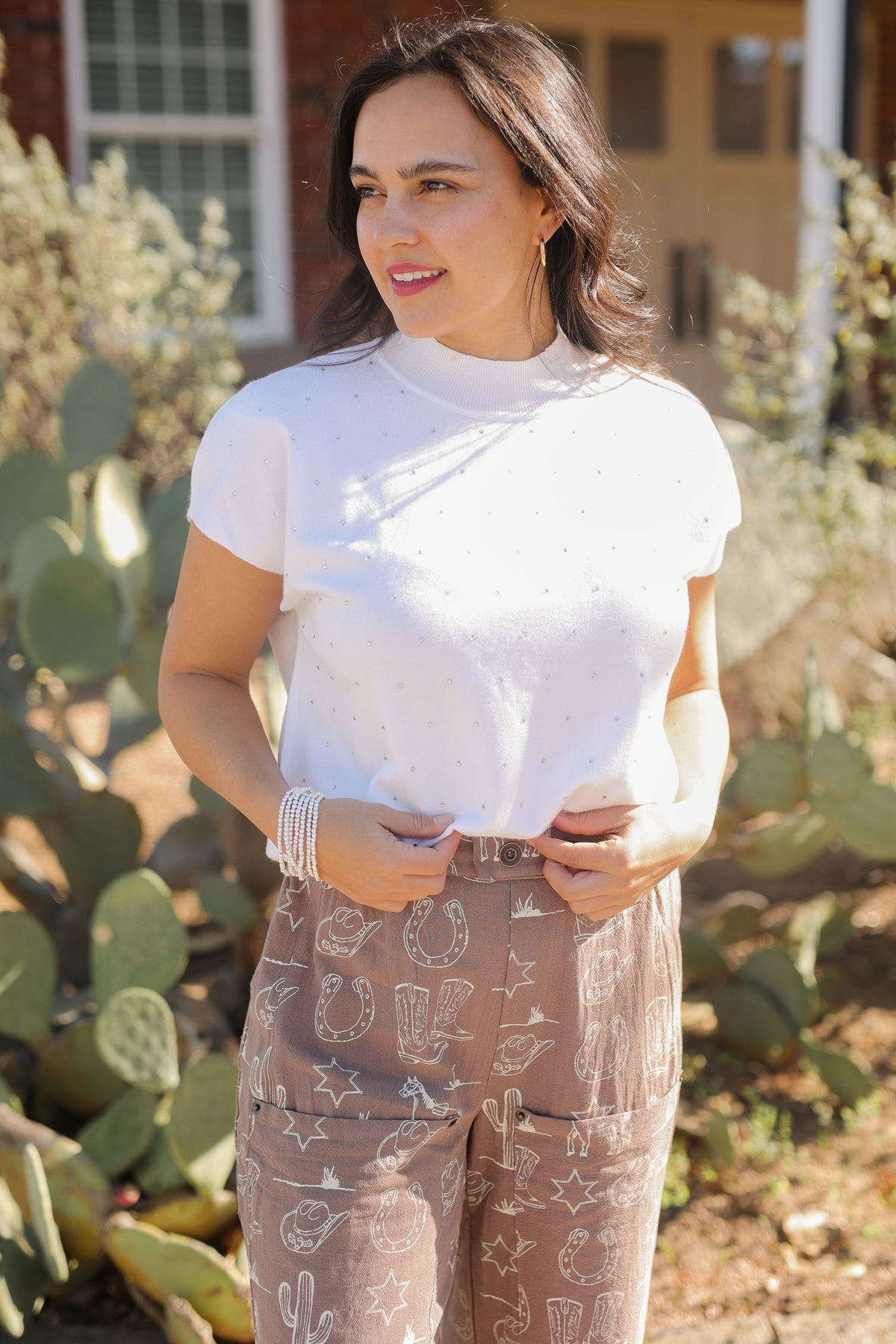 Woman wearing a white turtleneck and patterned pants standing in front of cacti.