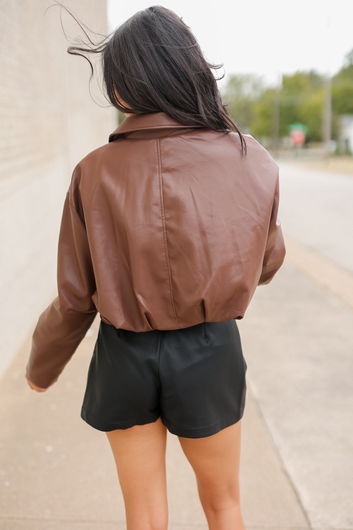 Model wearing the Riverton Cropped Faux Leather Jacket in Chocolate with the Briar black mini skirt and Amaya red western boots, featuring a relaxed silhouette and zip-front design. Southern House Clothing