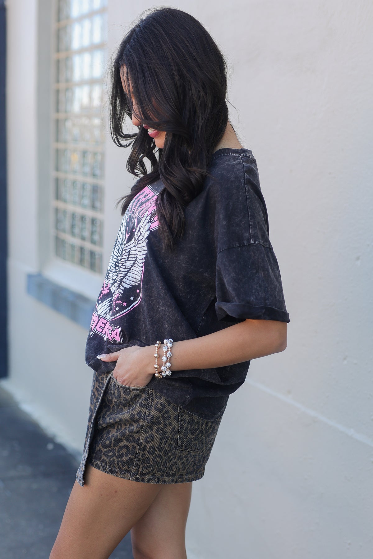 Woman wearing a graphic t-shirt and leopard print skirt against a white wall.