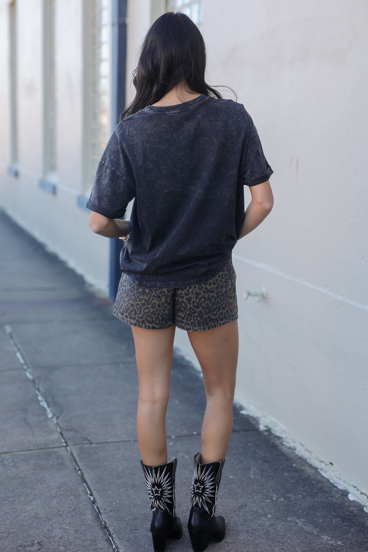 Person wearing a dark t-shirt, patterned shorts, and black boots on a sidewalk.