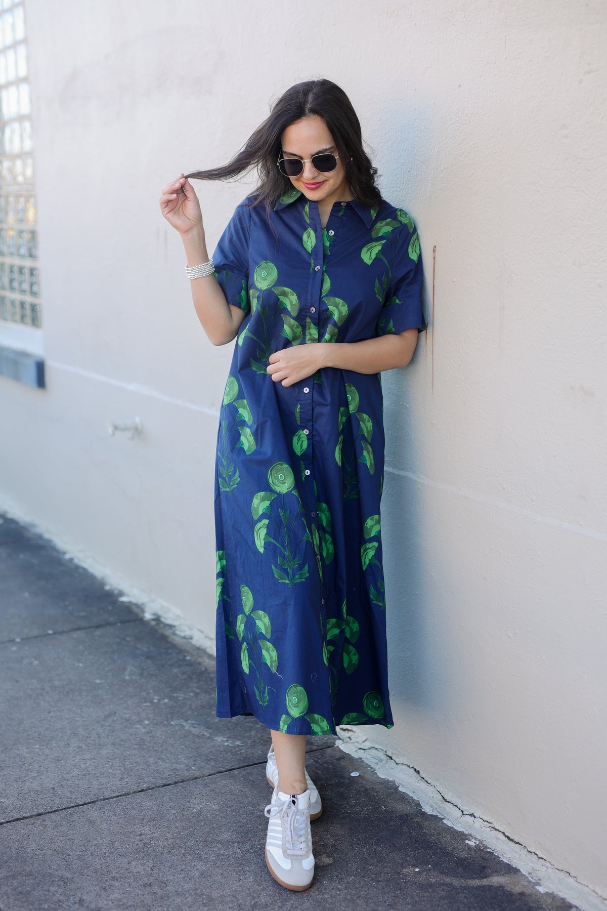 Woman wearing a blue dress with green patterns against a white wall.