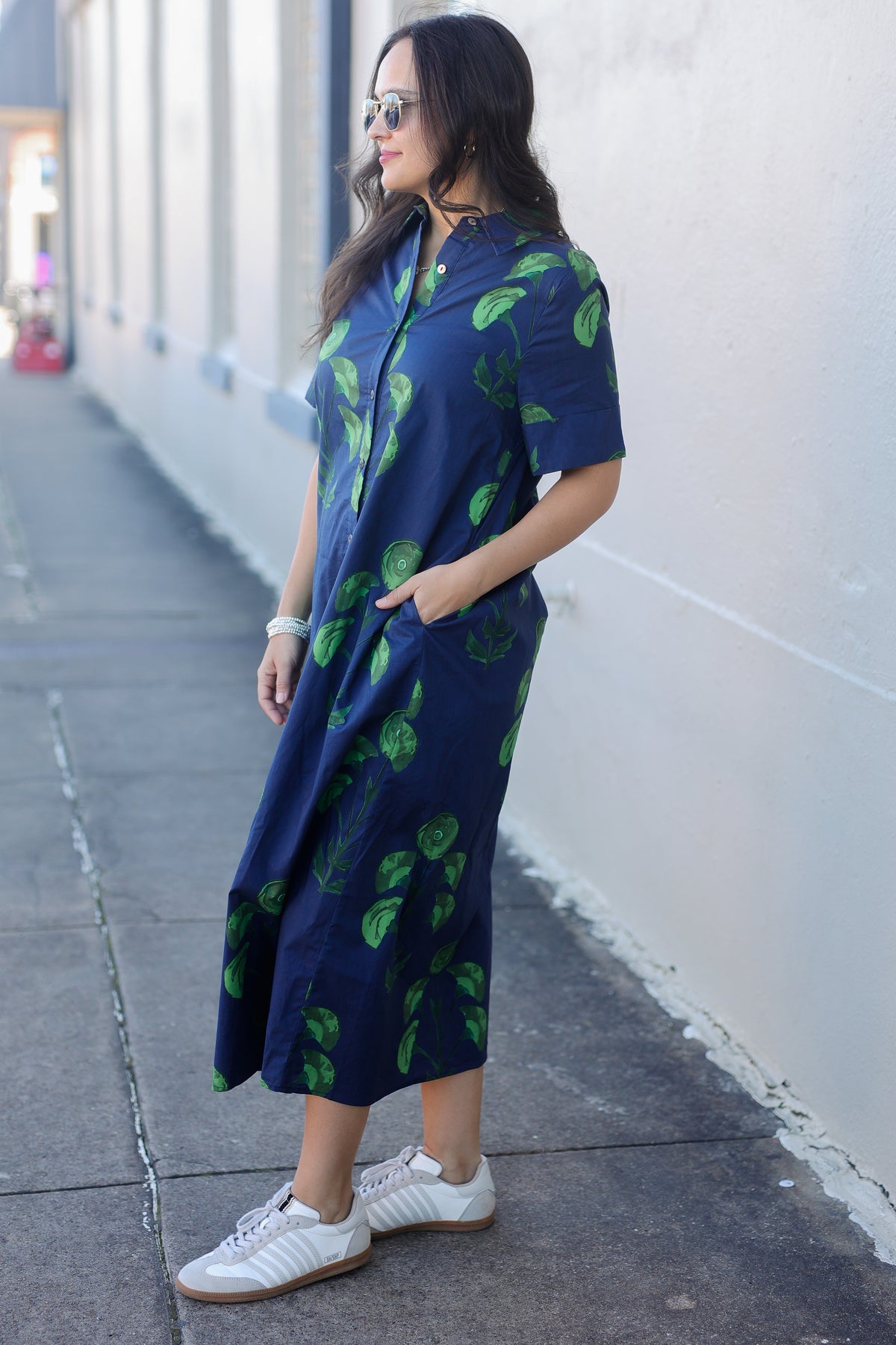 Woman wearing a navy dress with green leaf pattern standing on a sidewalk.
