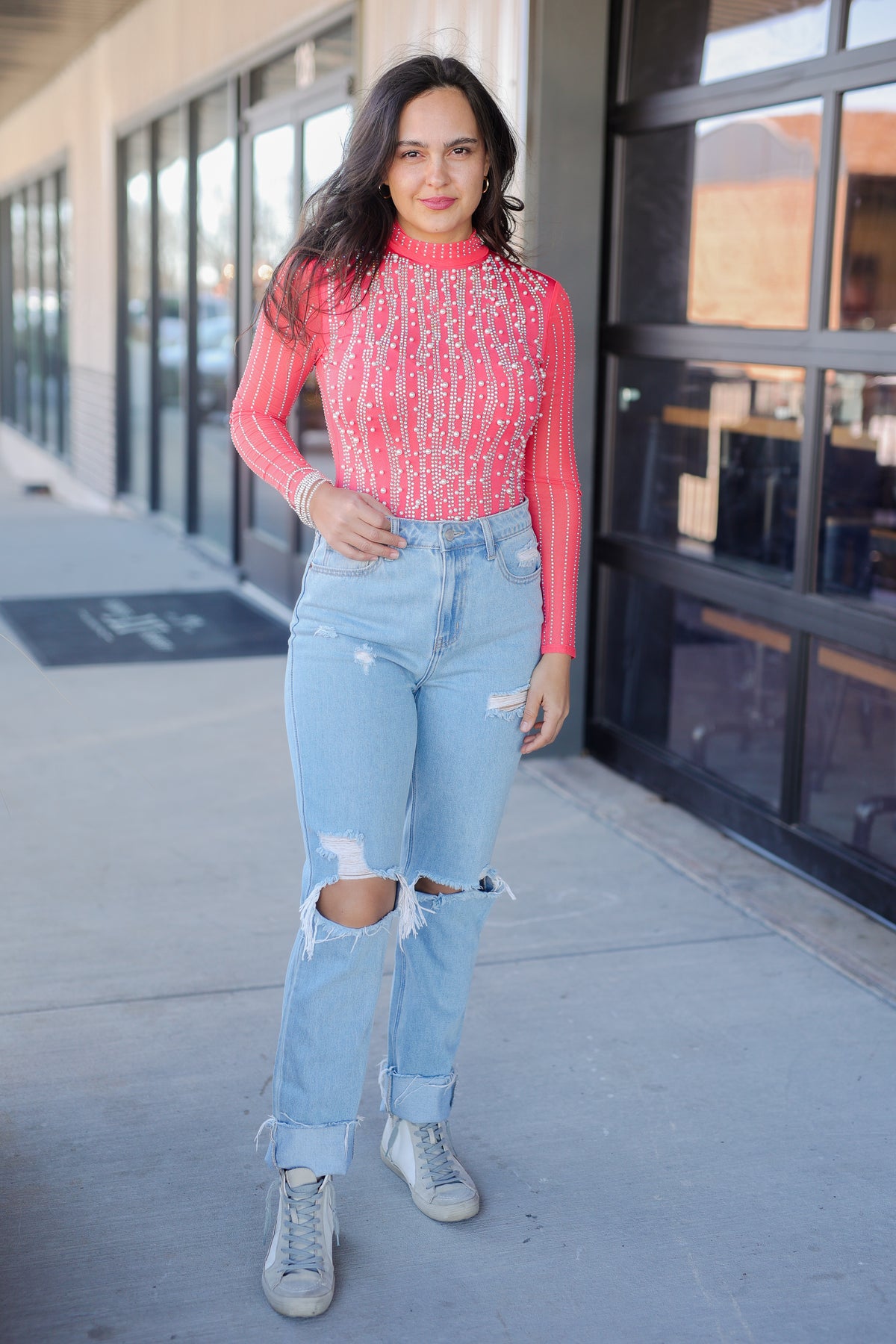 Woman wearing a pink sweater and light blue jeans standing outside a building.