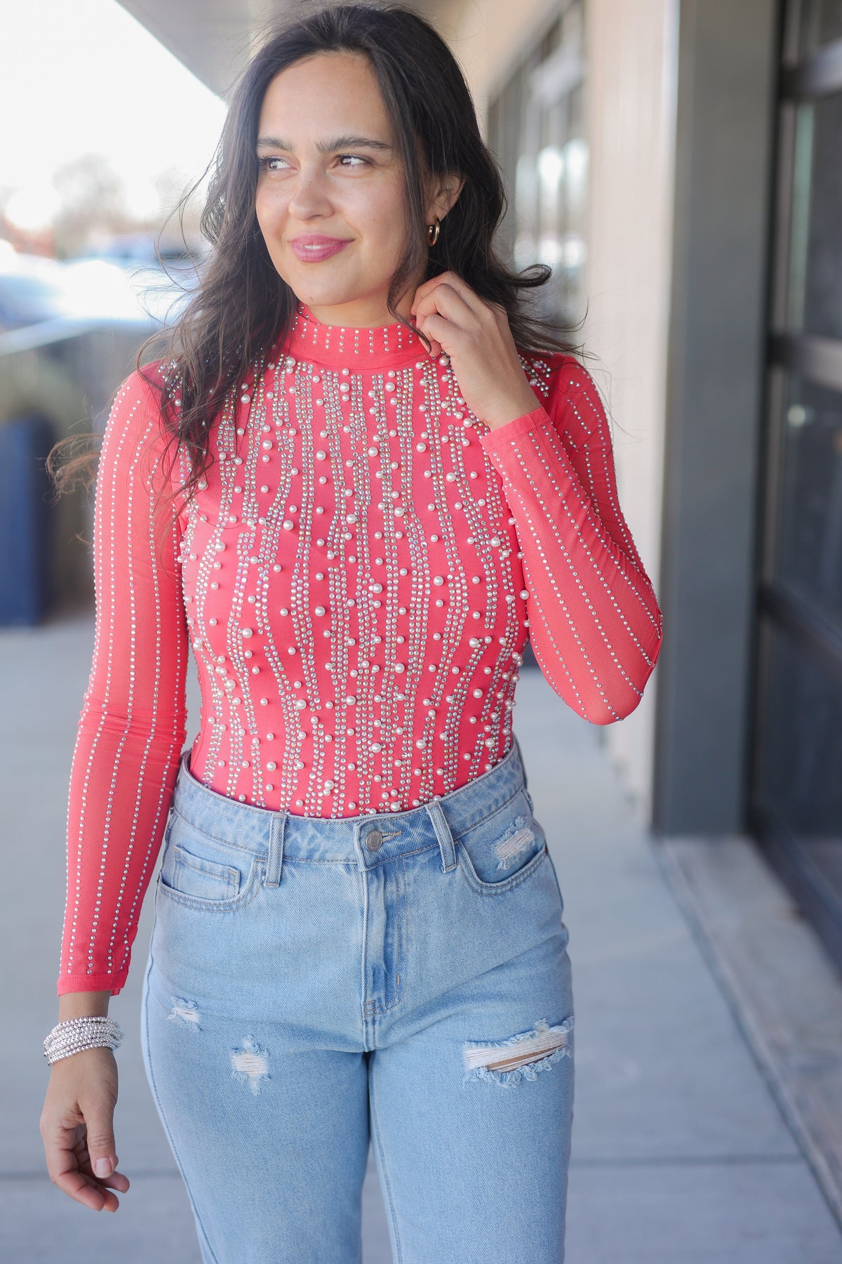 Woman wearing a red patterned top and light blue jeans outdoors.