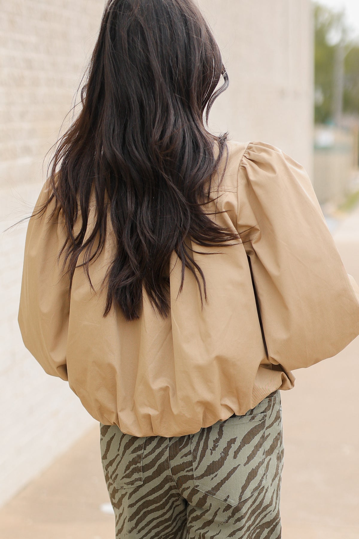 Back view of a model in the Winscott Puff Sleeve Zip Jacket in Khaki styled with Safari Stroll Wide Leg Pants in olive animal print and metallic gold ballet flats, showing the cropped fit and puff sleeves. Southern House Clothing