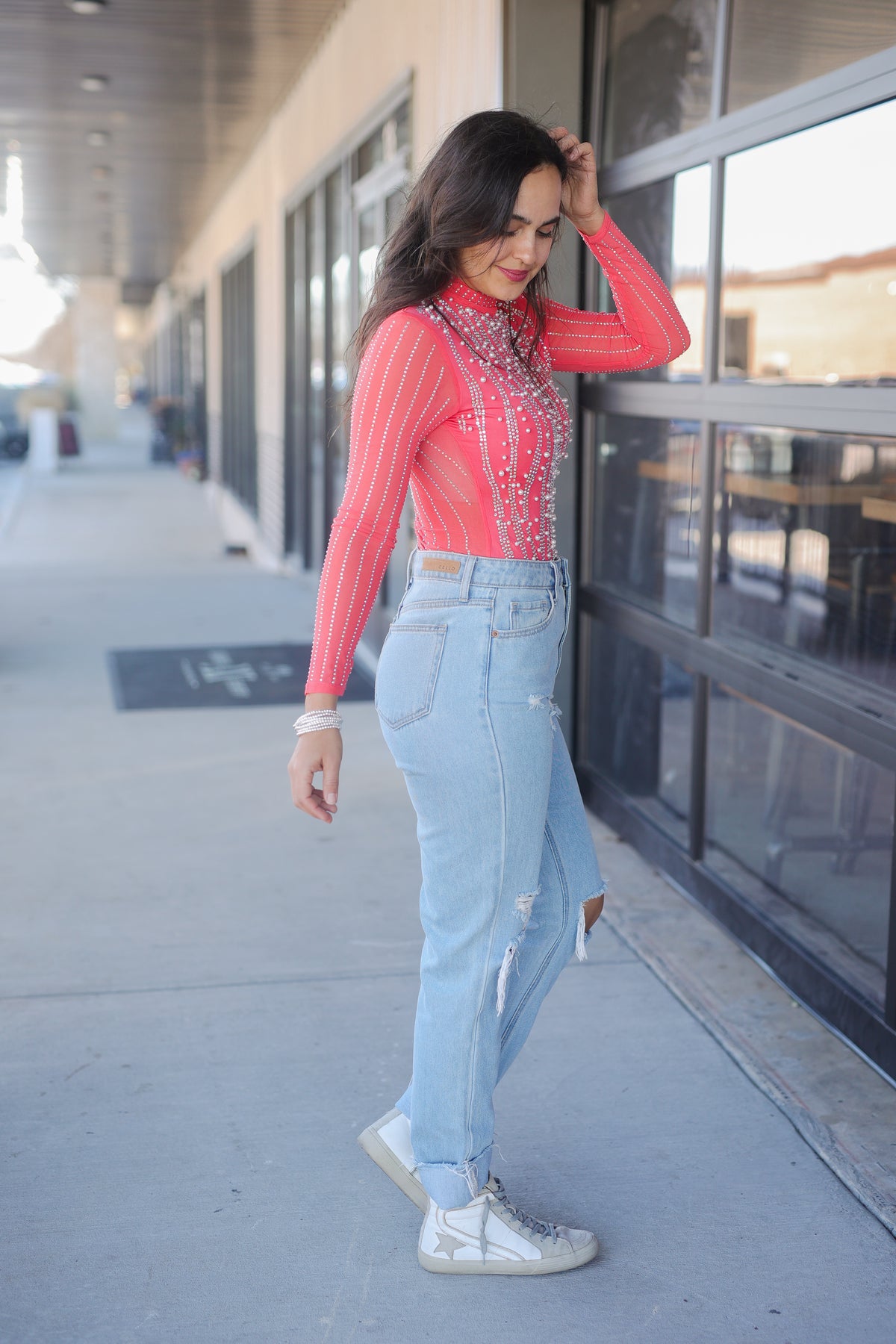 Woman wearing a red striped shirt and light blue jeans standing on a sidewalk.