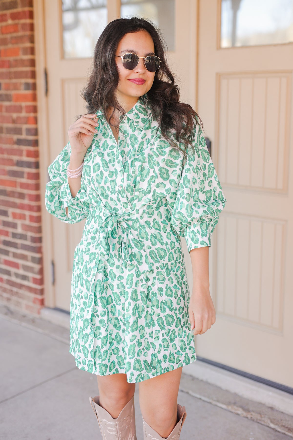 Woman wearing a green leopard print dress with sunglasses outdoors.