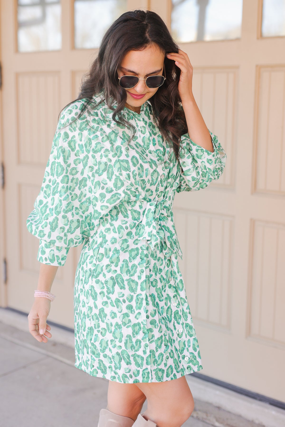 Woman wearing a green leopard print dress with sunglasses indoors.