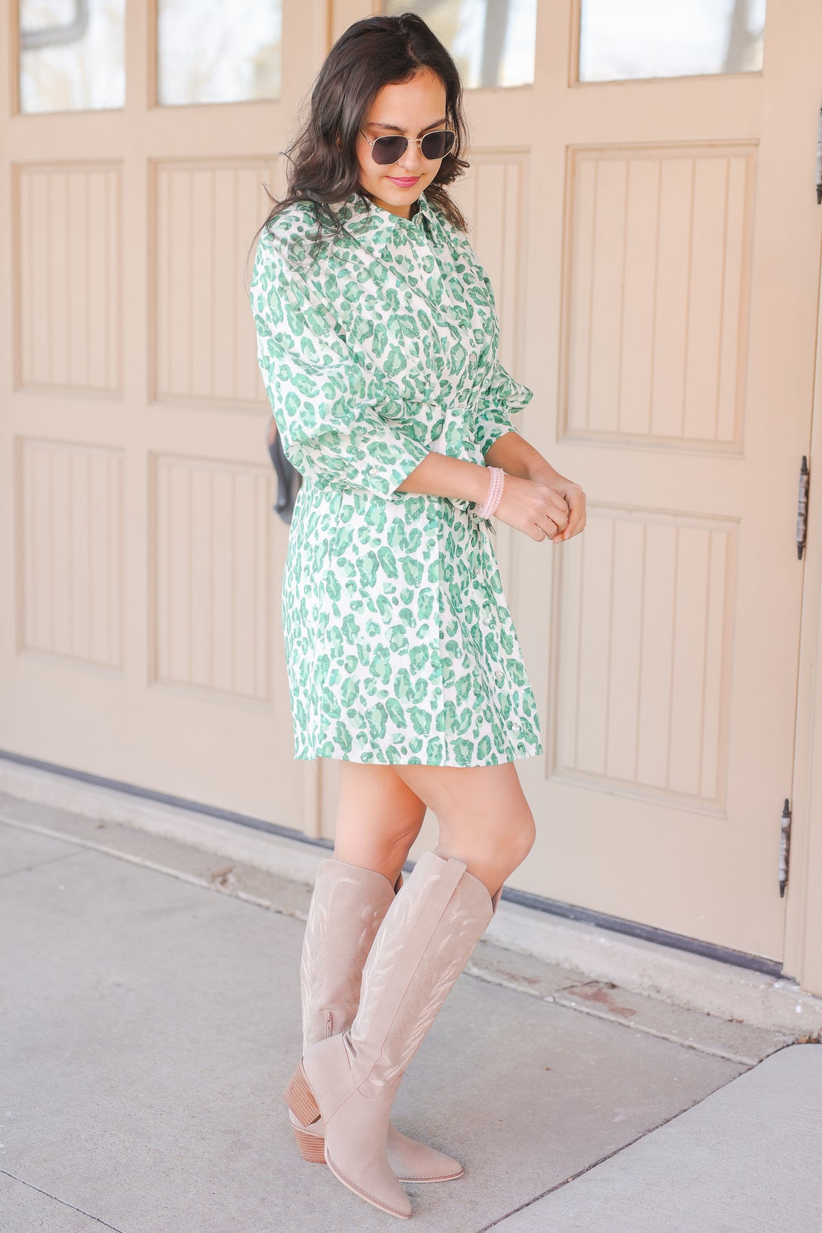 Woman wearing a green floral dress and beige knee-high boots standing in front of a garage door.