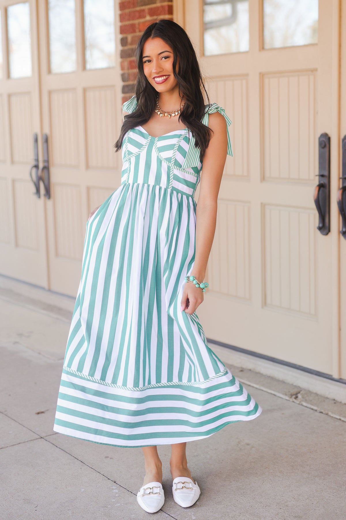 Woman wearing a green and white striped dress standing in front of a wooden door.