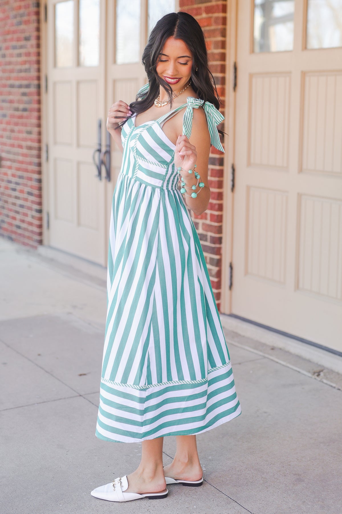Woman wearing a green and white striped dress with a bow detail, standing in front of a garage door.