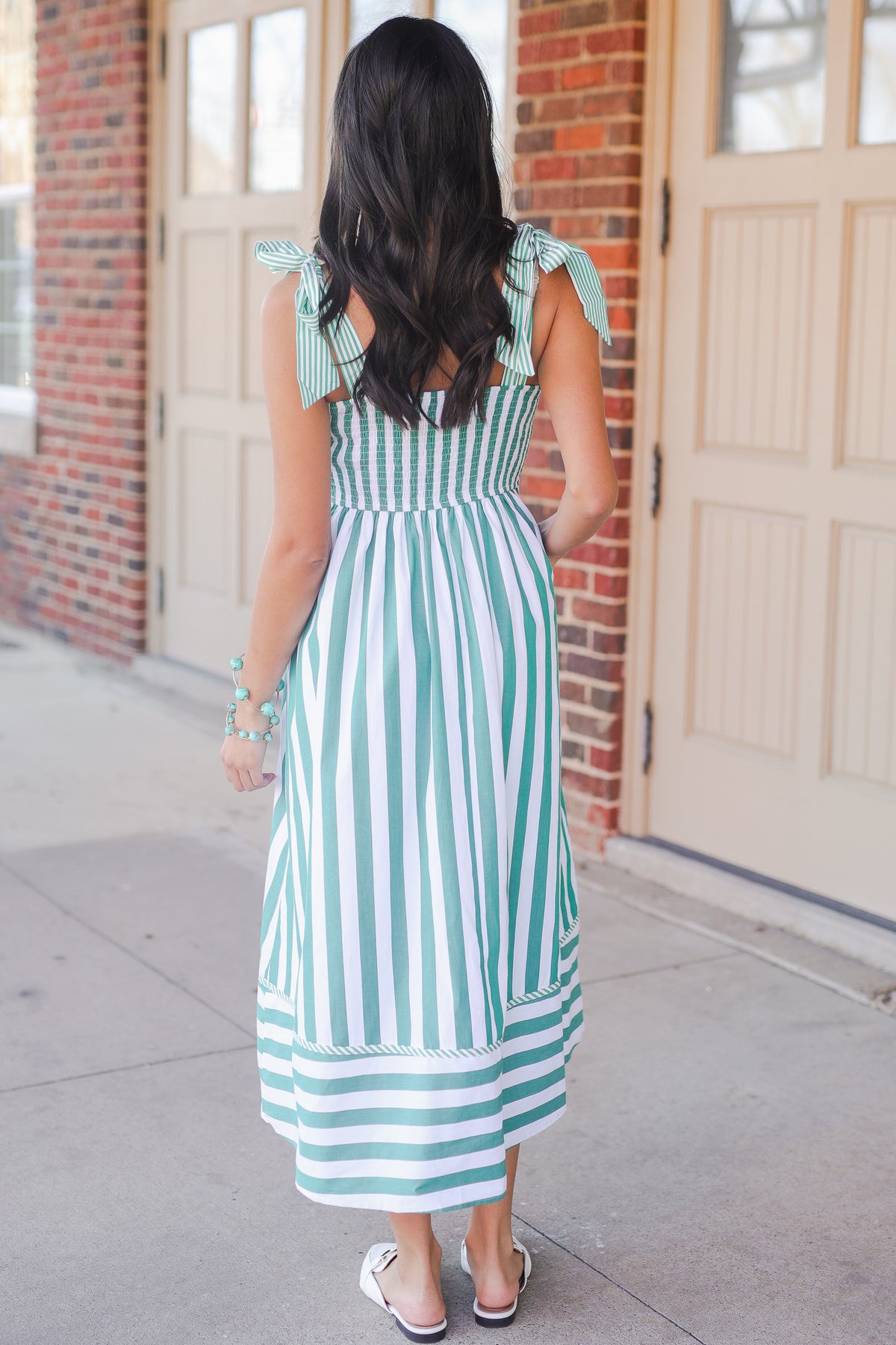 Woman wearing a green and white striped dress standing in front of a brick building.