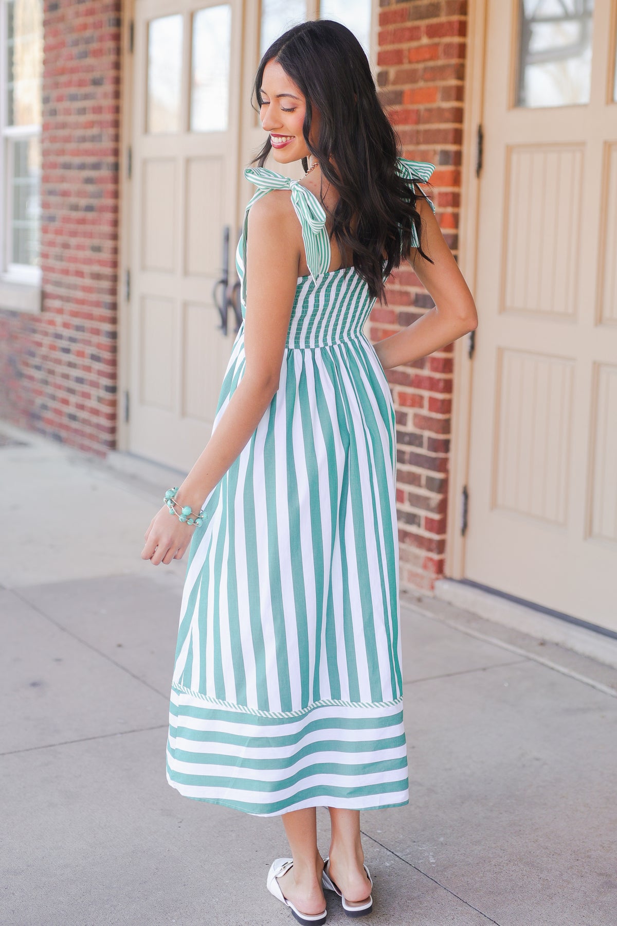 Woman wearing a green and white striped dress standing on a sidewalk.
