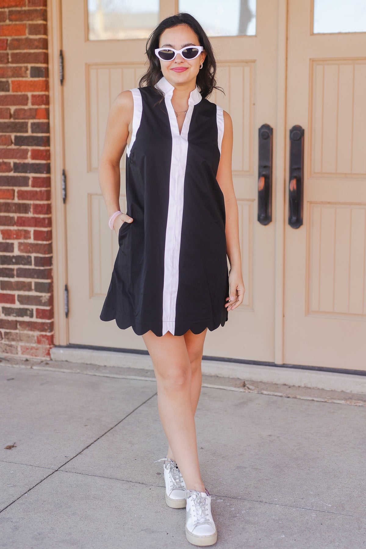 Woman wearing a black and white dress with sunglasses standing in front of double doors.