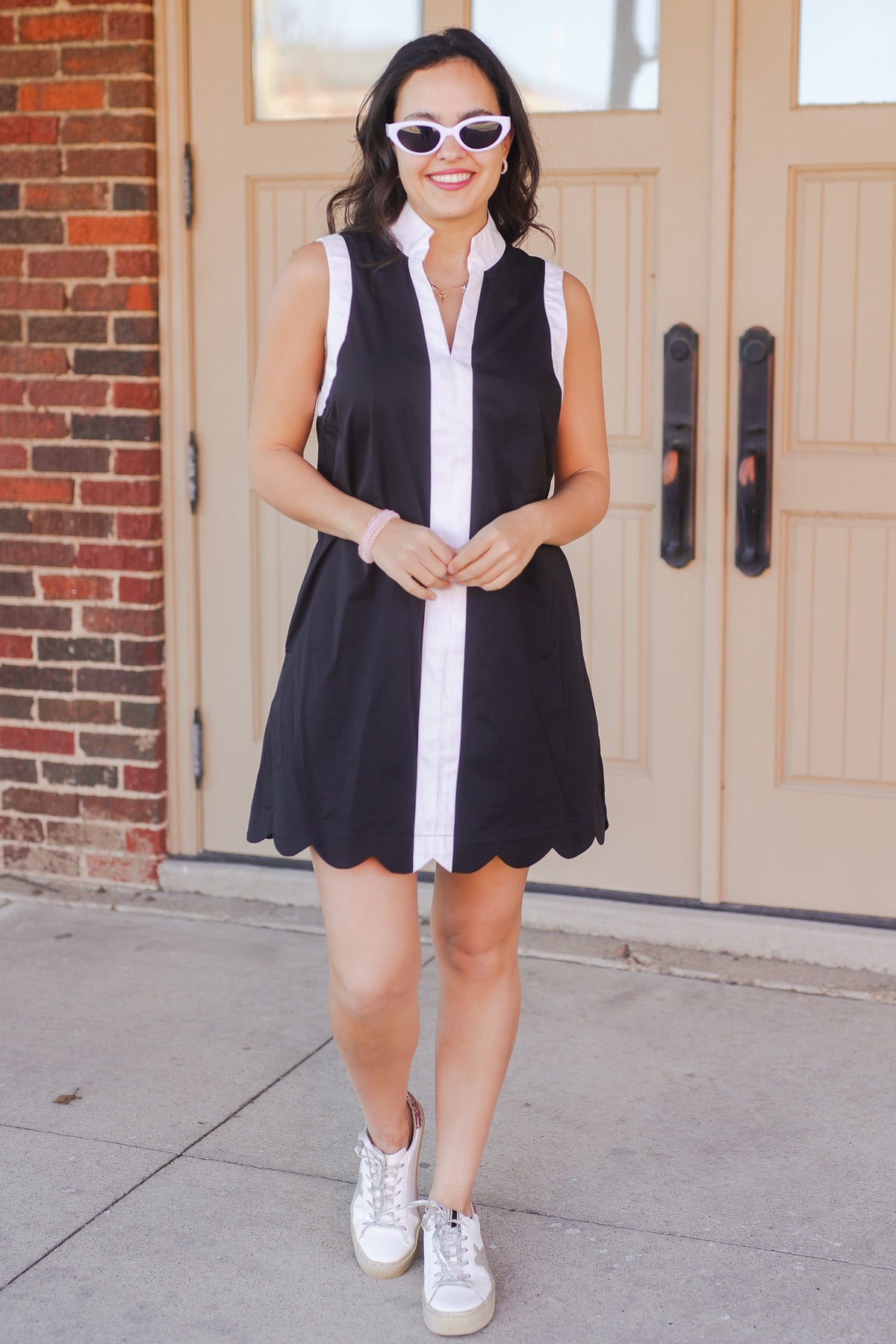 Woman wearing a black and white dress with sunglasses standing in front of a building.