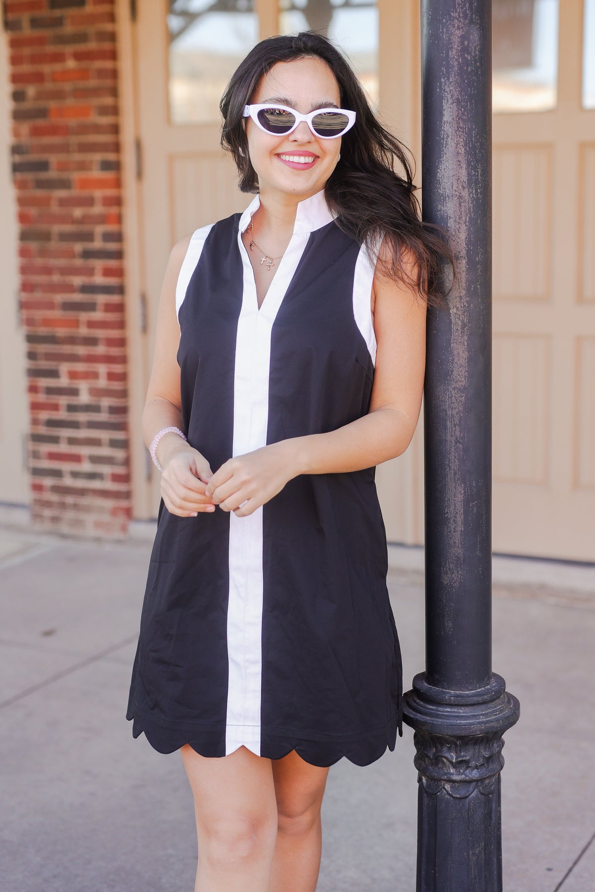 Woman wearing a black and white dress standing next to a pole.