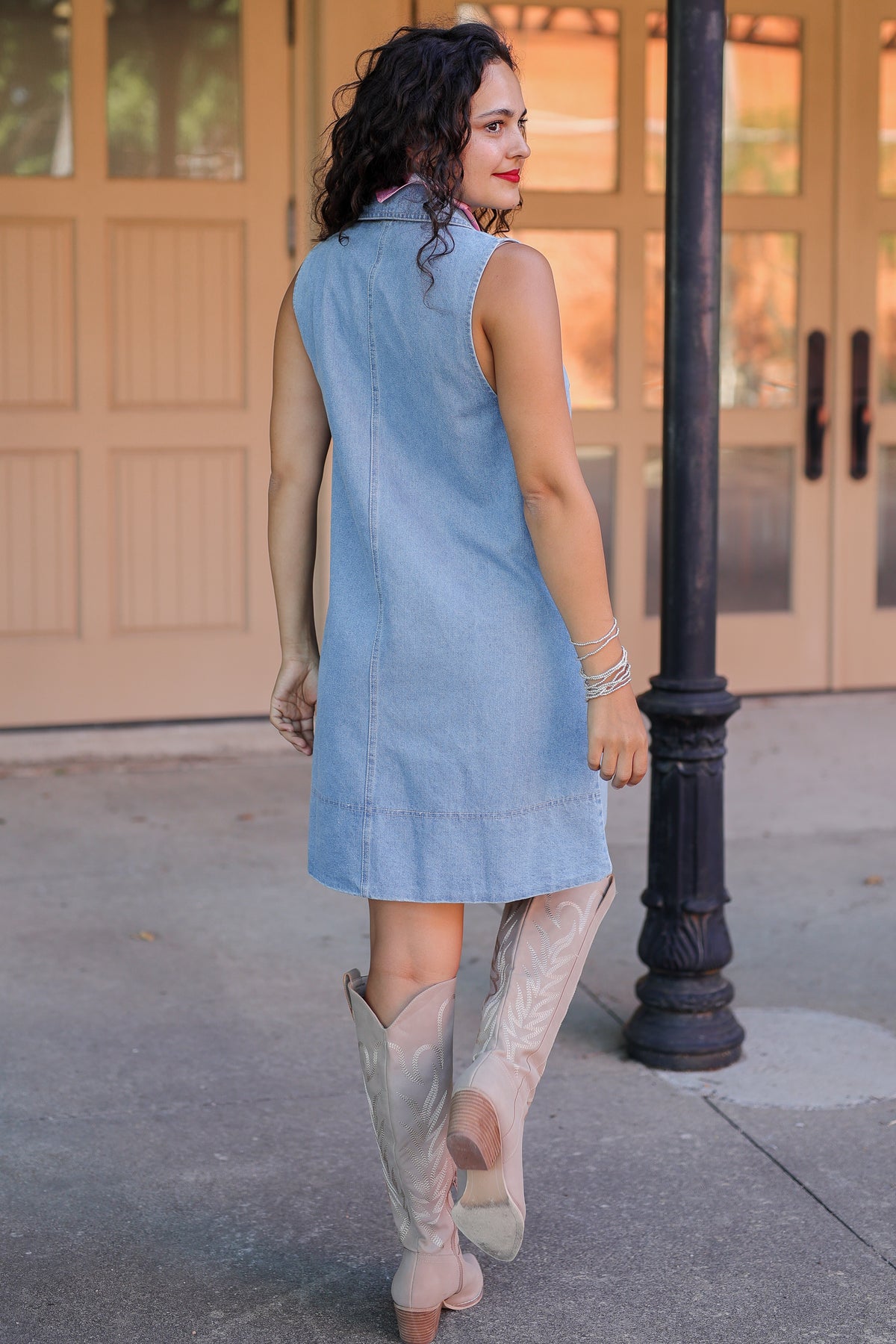 Woman in a denim dress and beige boots walking outdoors.