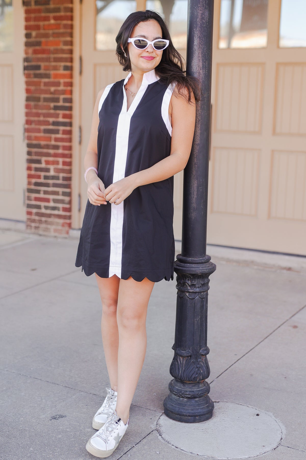 Woman in a black and white dress standing next to a lamp post on a sidewalk.