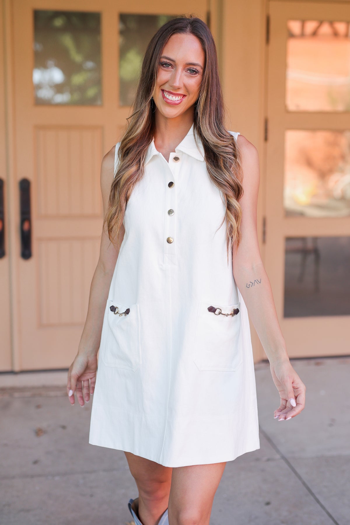 Woman wearing a white sleeveless dress with buttons in front of a beige door.