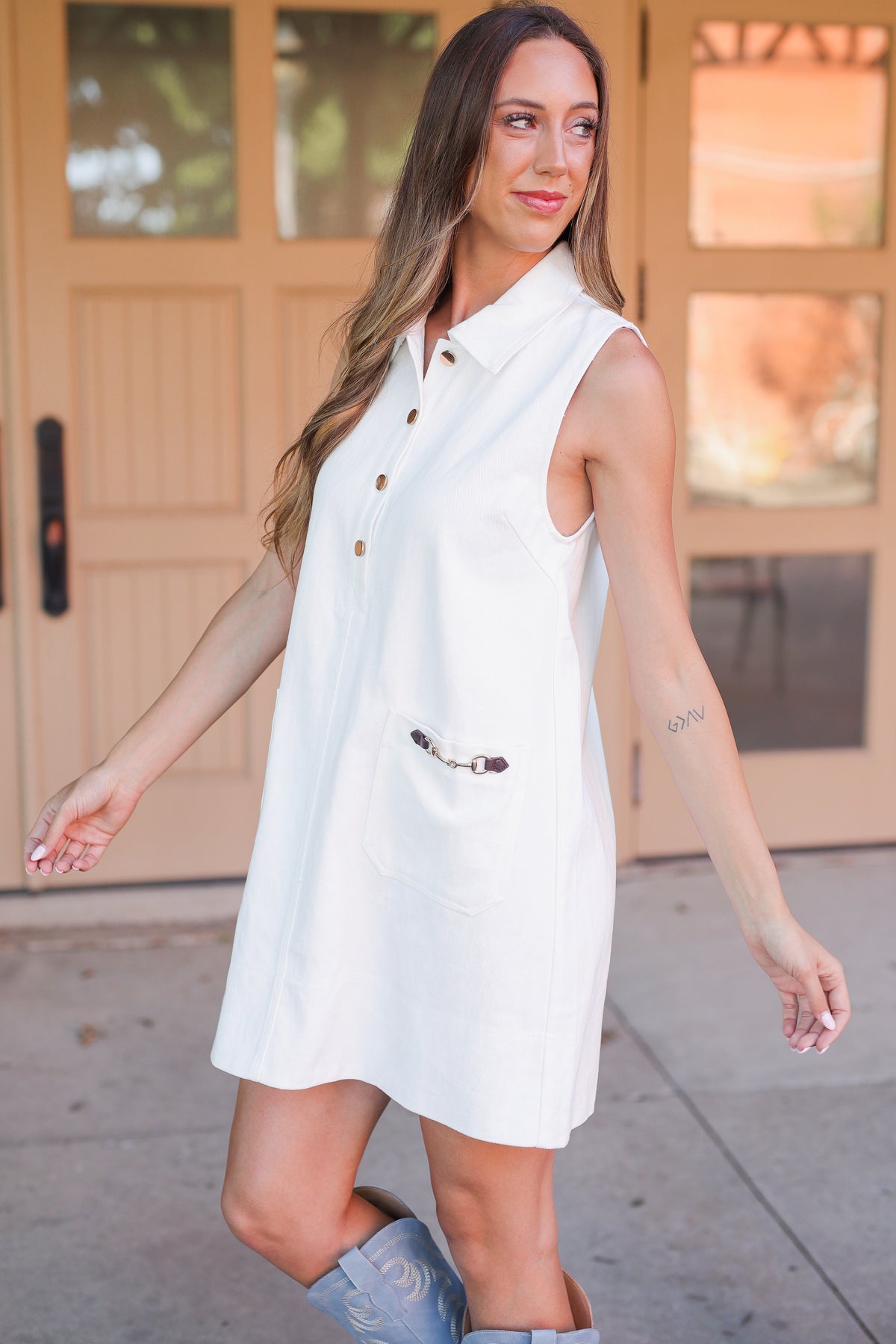 Woman wearing a white sleeveless dress with buttons, standing on a sidewalk.