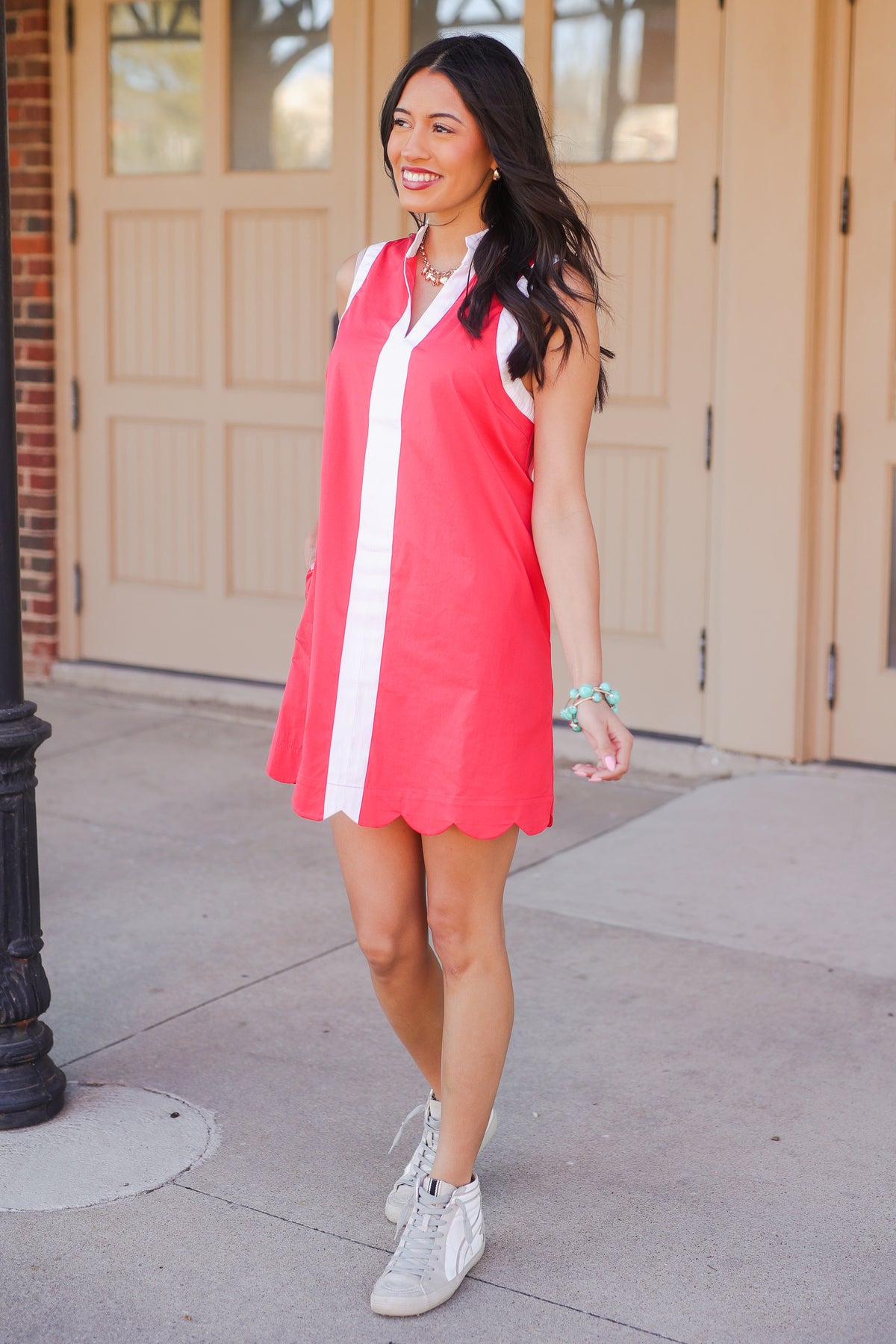 Woman wearing a pink dress with white accents standing on a sidewalk.