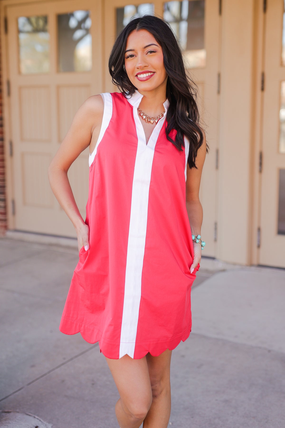 Woman wearing a red dress with a white stripe standing outdoors.