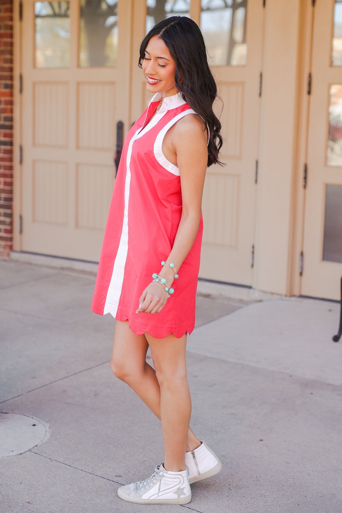 Woman wearing a red and white dress with sneakers standing on a sidewalk.