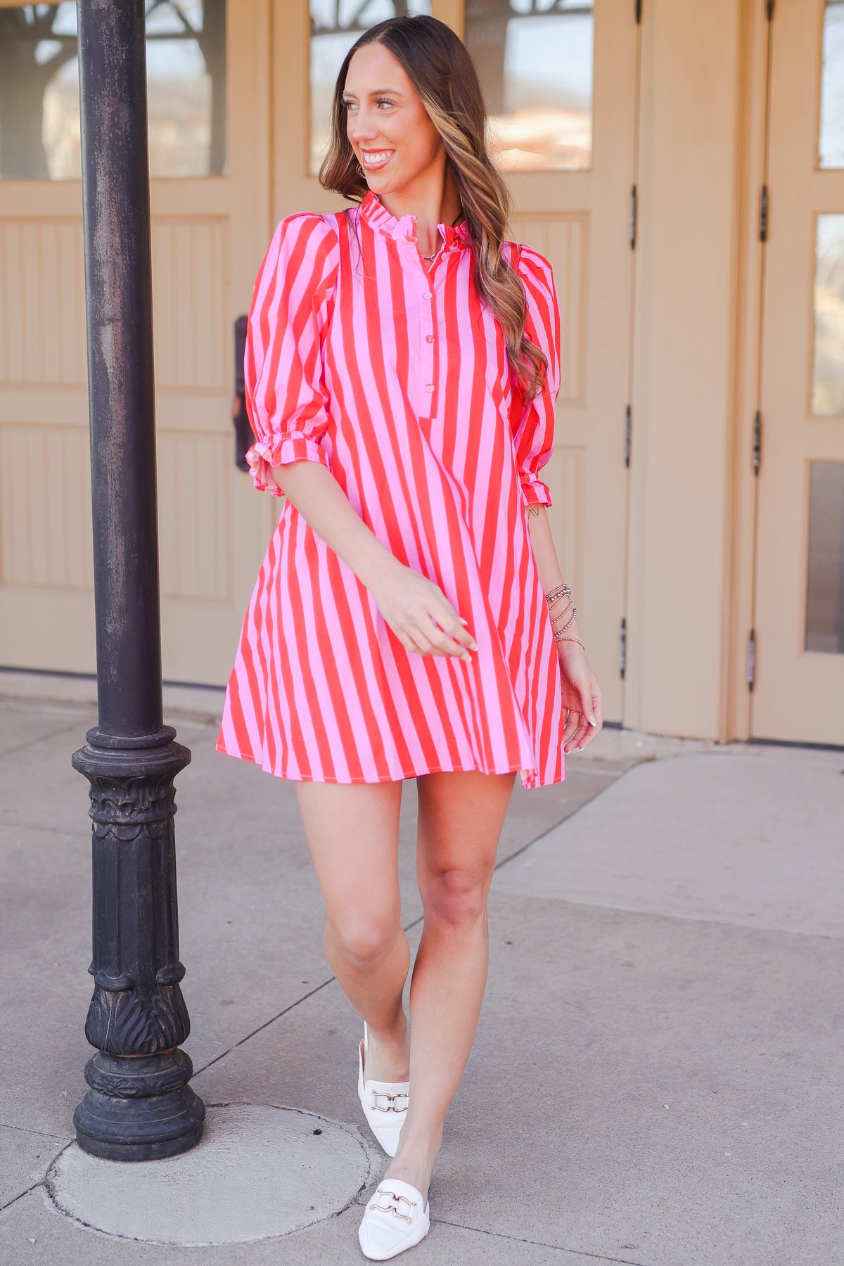Woman in a pink and red striped dress standing outside.