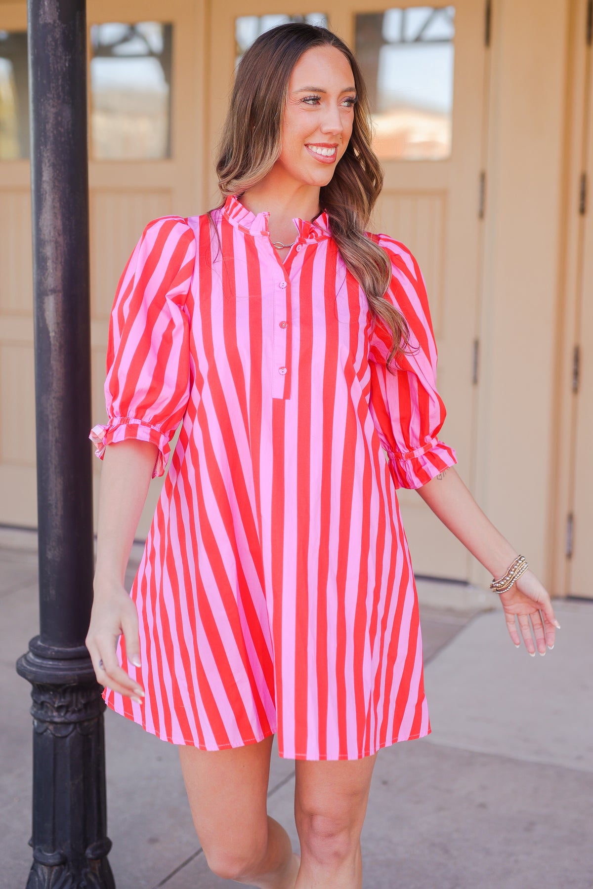 Woman in a pink and red striped dress standing outside.