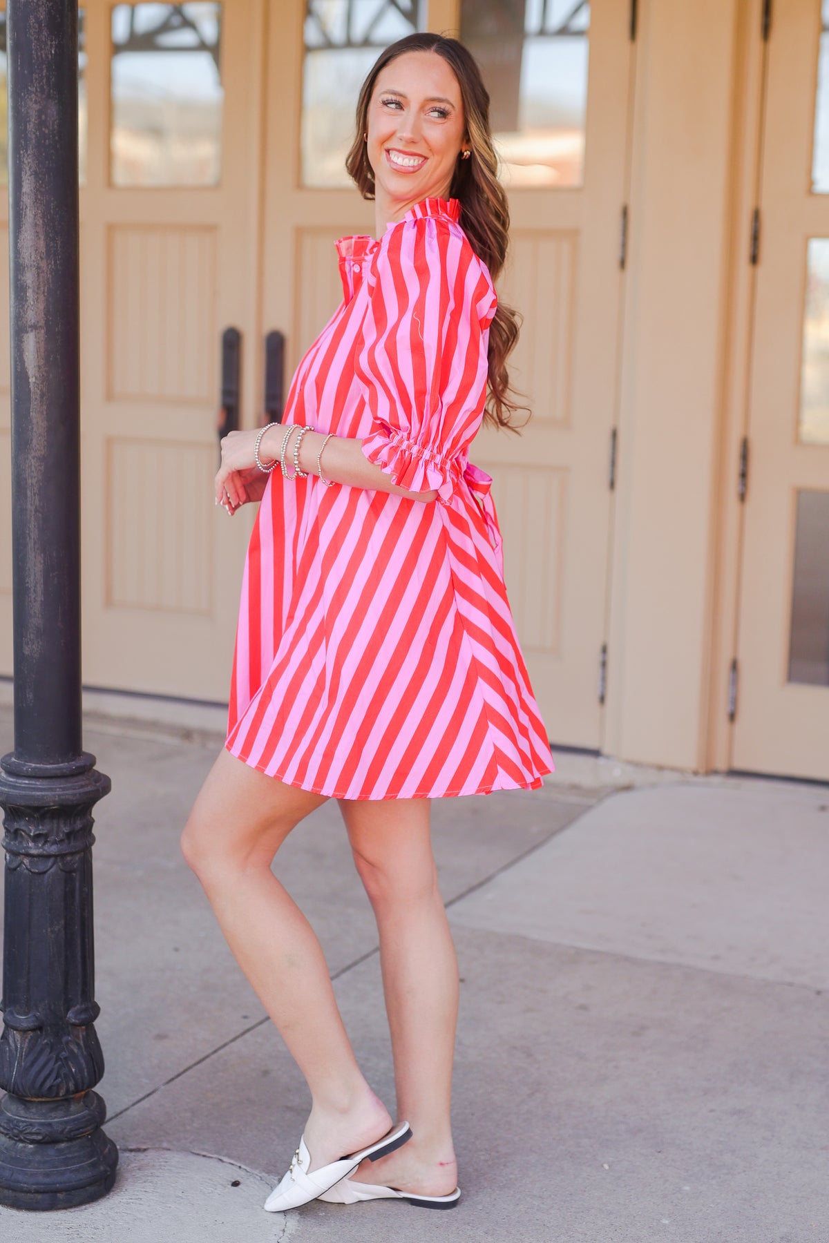 Woman in a pink and red striped dress standing outside.
