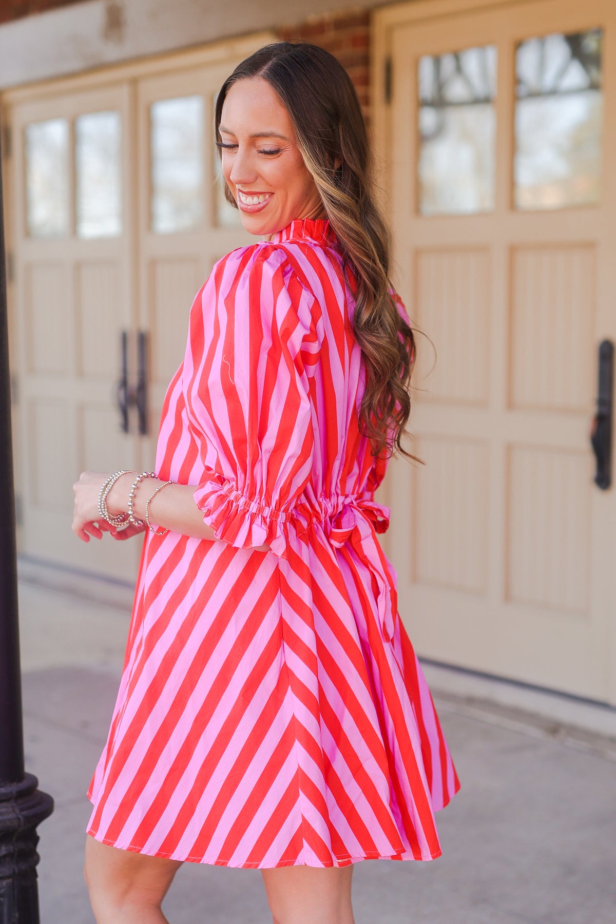 Woman in a pink and red striped dress standing outside.
