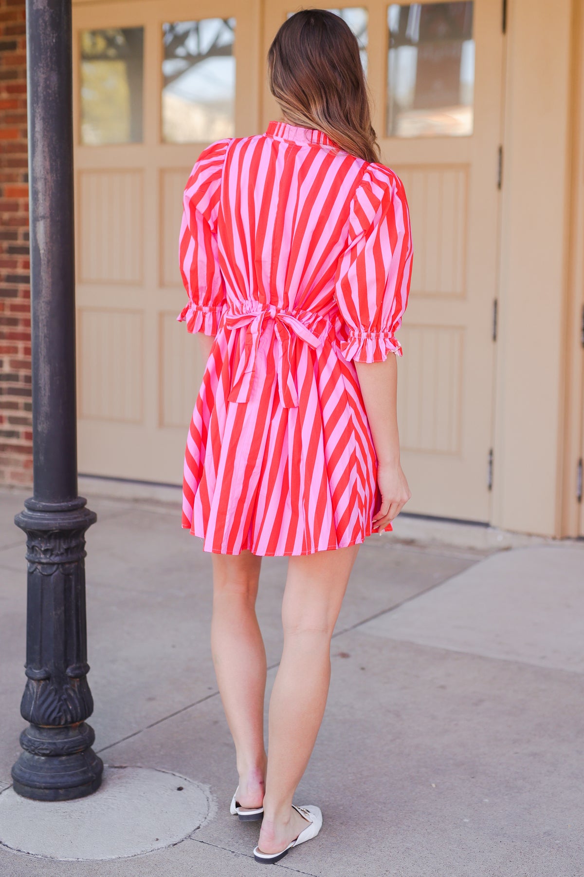 Woman in a pink and red striped dress standing outside.
