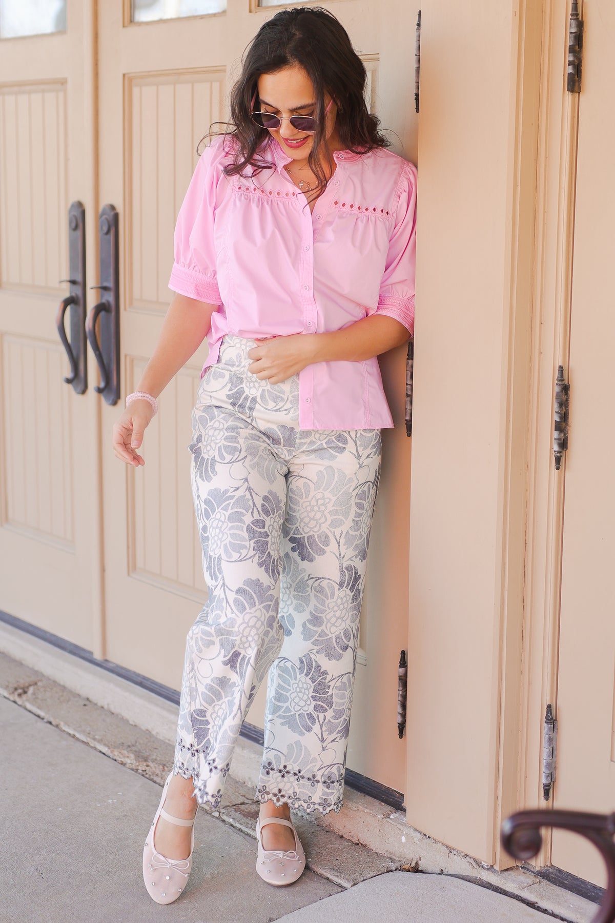 Woman wearing a pink blouse with white floral pants outside.