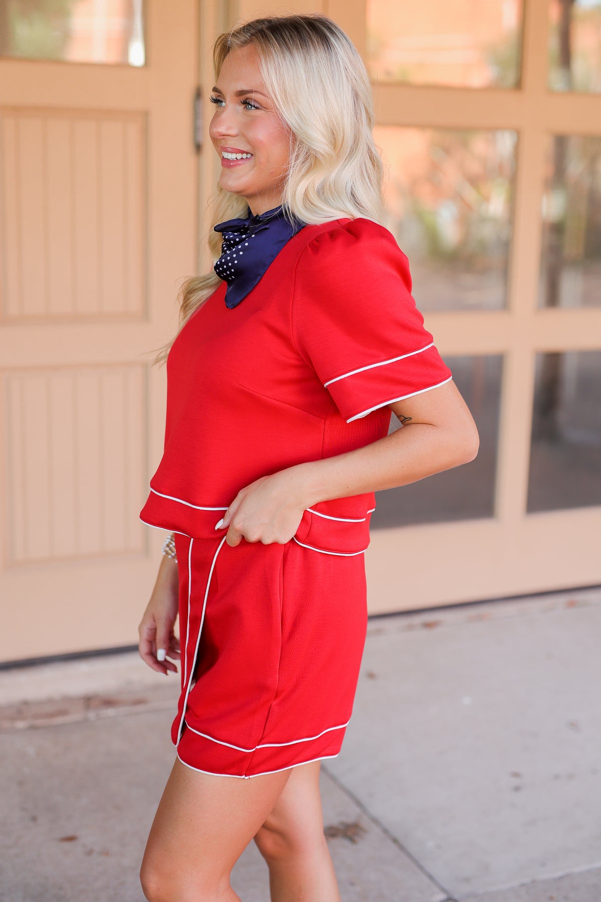 Woman wearing a red outfit with white trim standing in front of a glass door.
