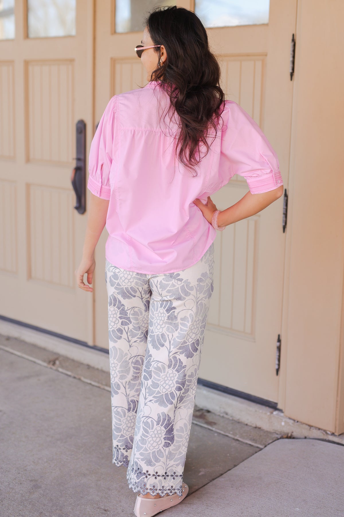Woman wearing a pink blouse with white floral pants outside.
