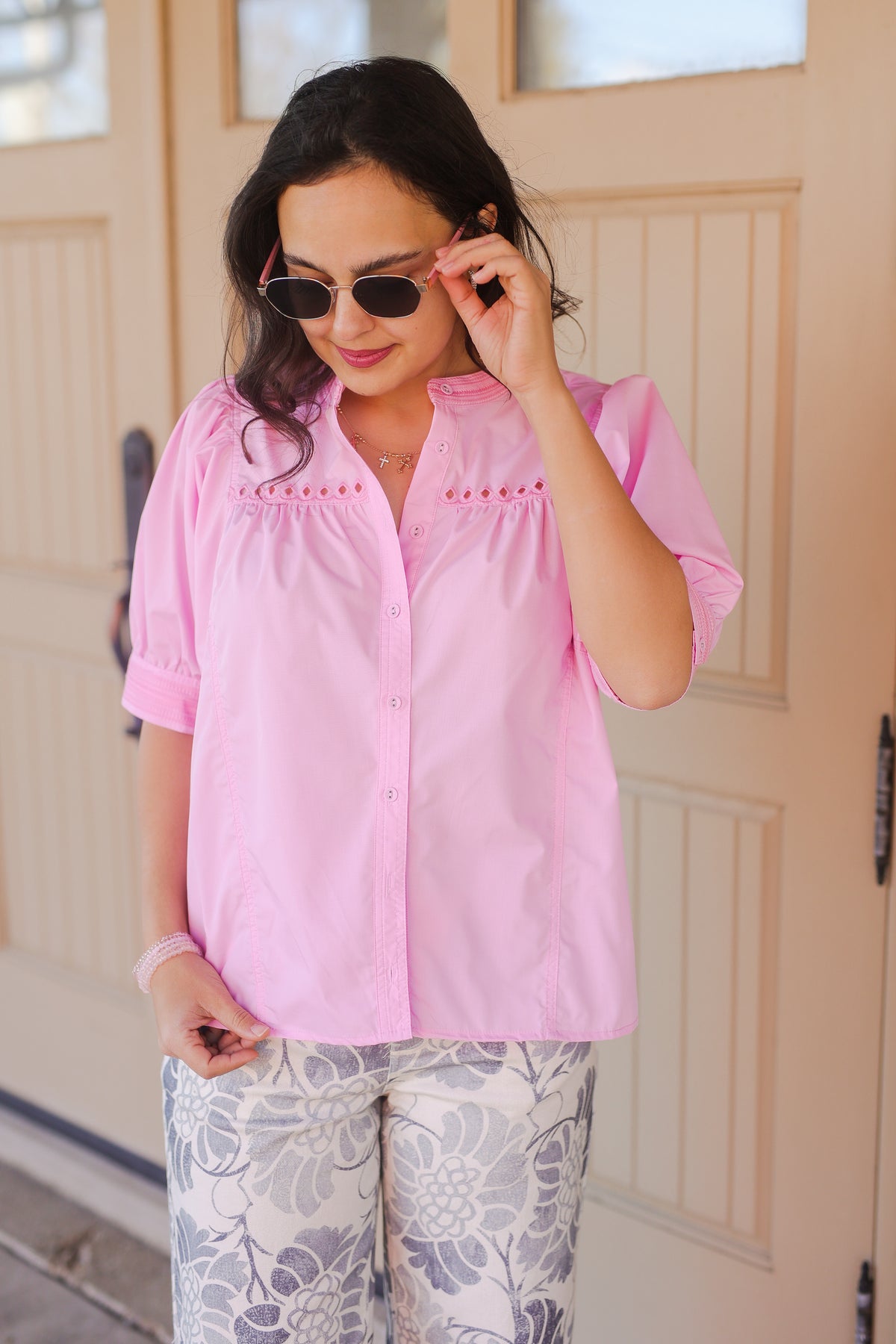 Woman wearing a pink blouse with white floral pants outside.