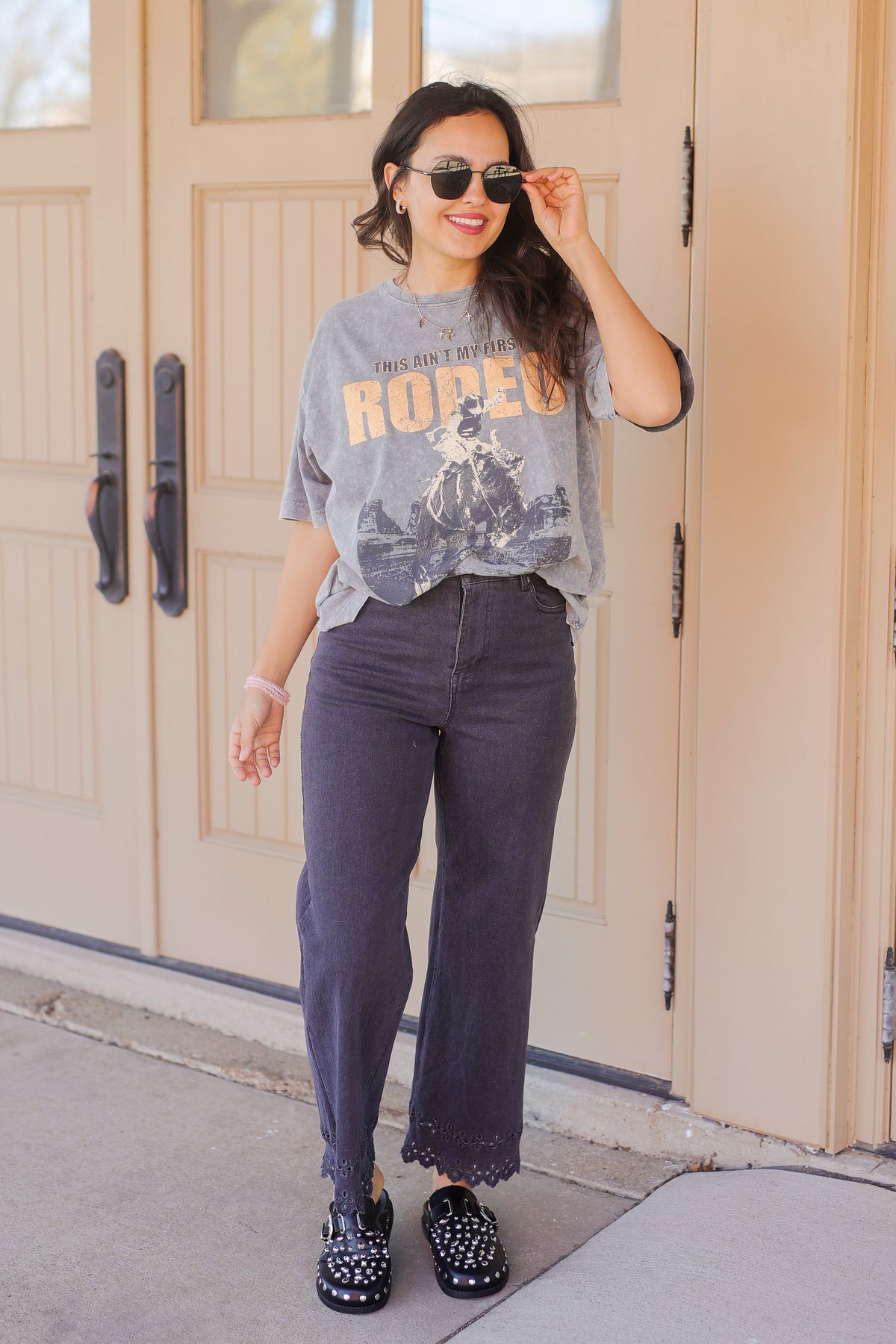 Woman wearing a graphic t-shirt and jeans standing in front of a wooden door.