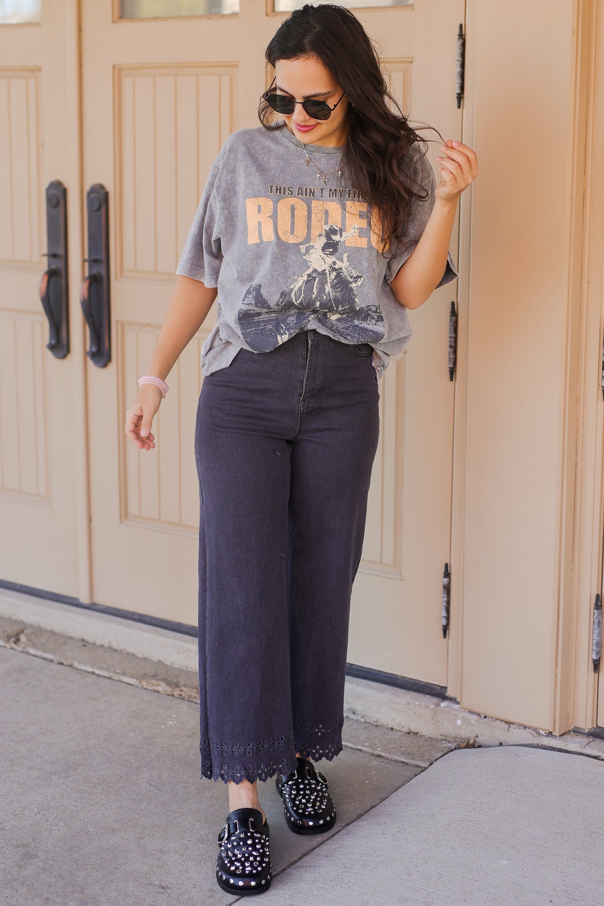 Woman wearing a graphic t-shirt and dark jeans standing in front of a door.