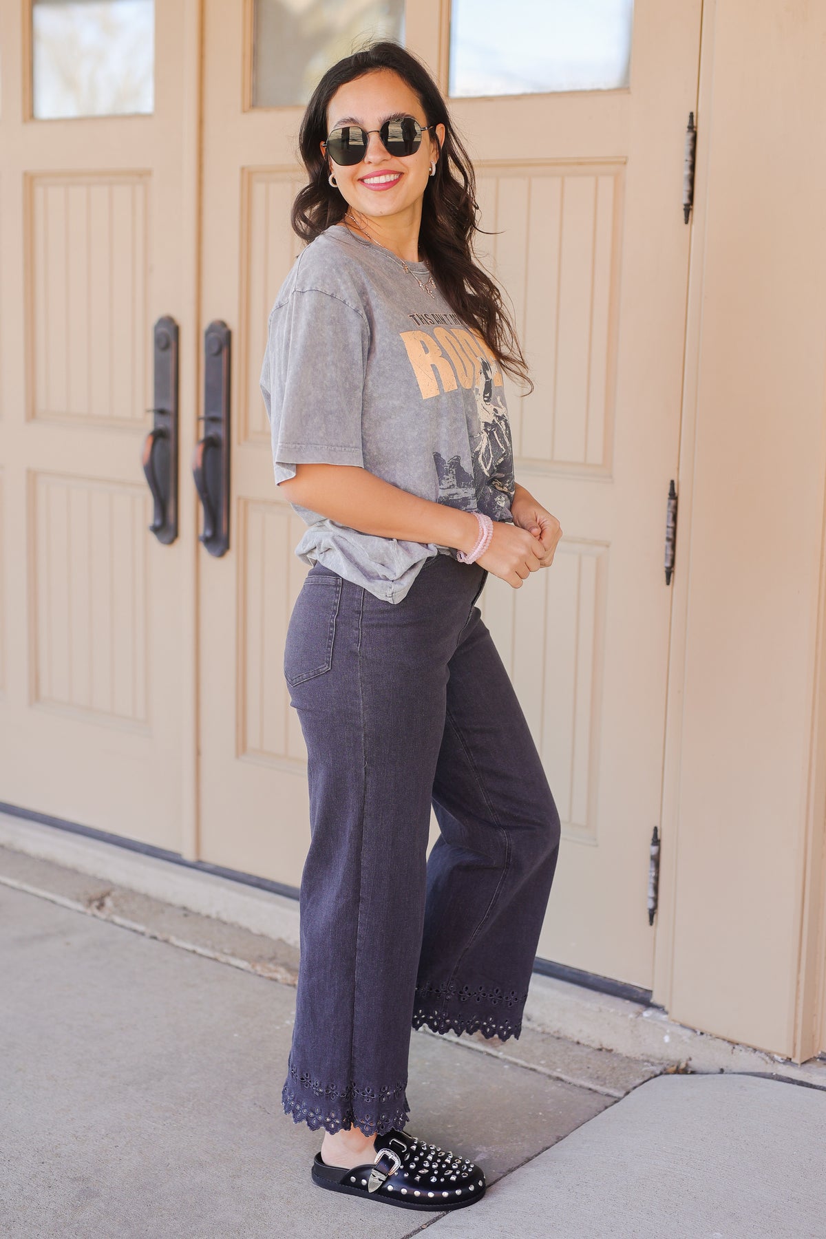Woman wearing a gray t-shirt and dark pants standing in front of a beige door.