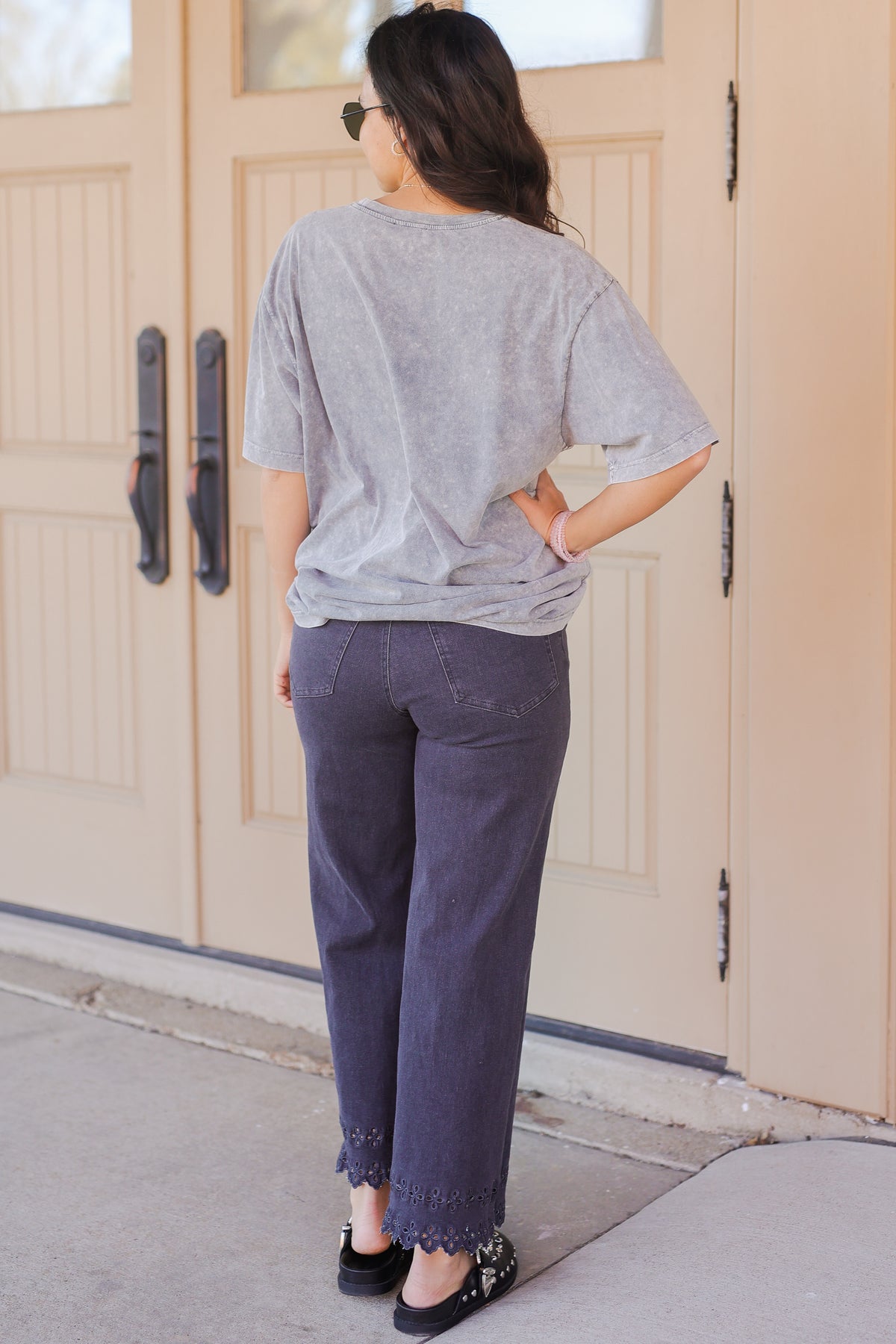 Person wearing a gray t-shirt and purple pants standing in front of a beige door.
