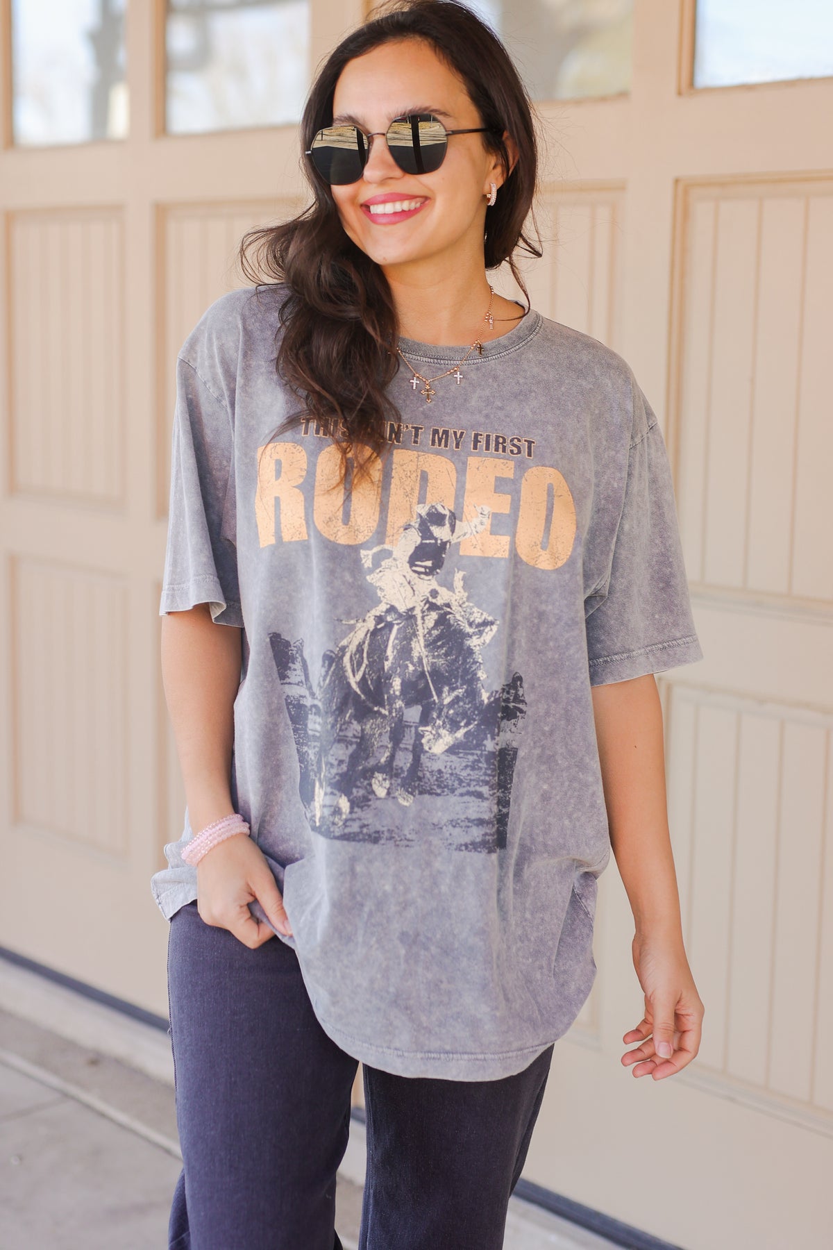Woman wearing a gray graphic t-shirt with text and a graphic design, standing in front of a wooden door.