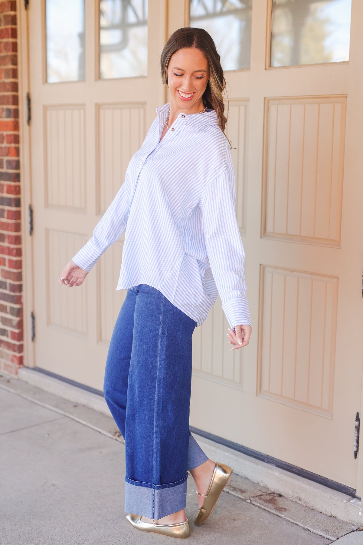 Woman wearing a white and blue striped shirt and blue jeans standing in front of a garage door.