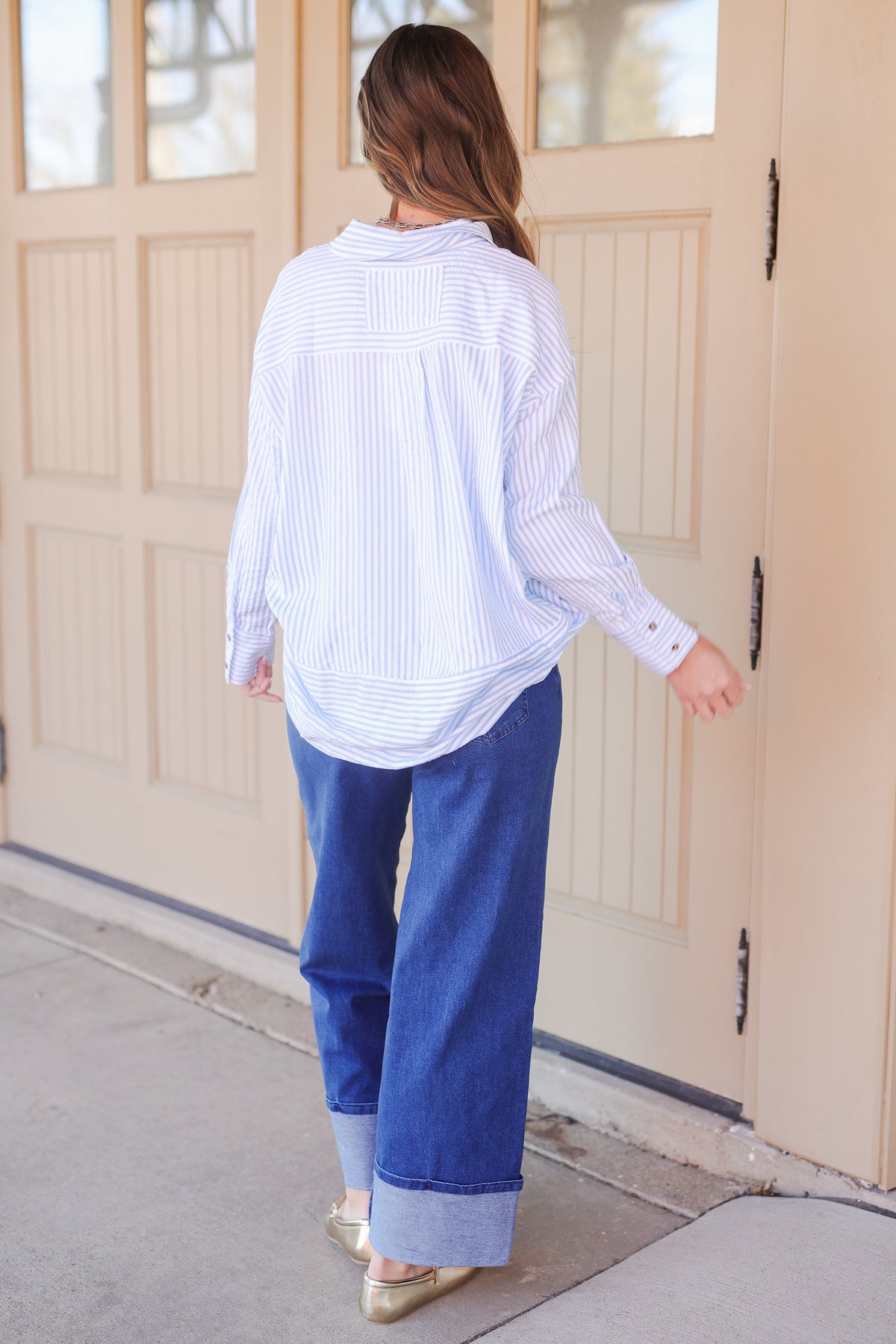 Person wearing a white striped shirt and blue pants standing in front of a beige door.