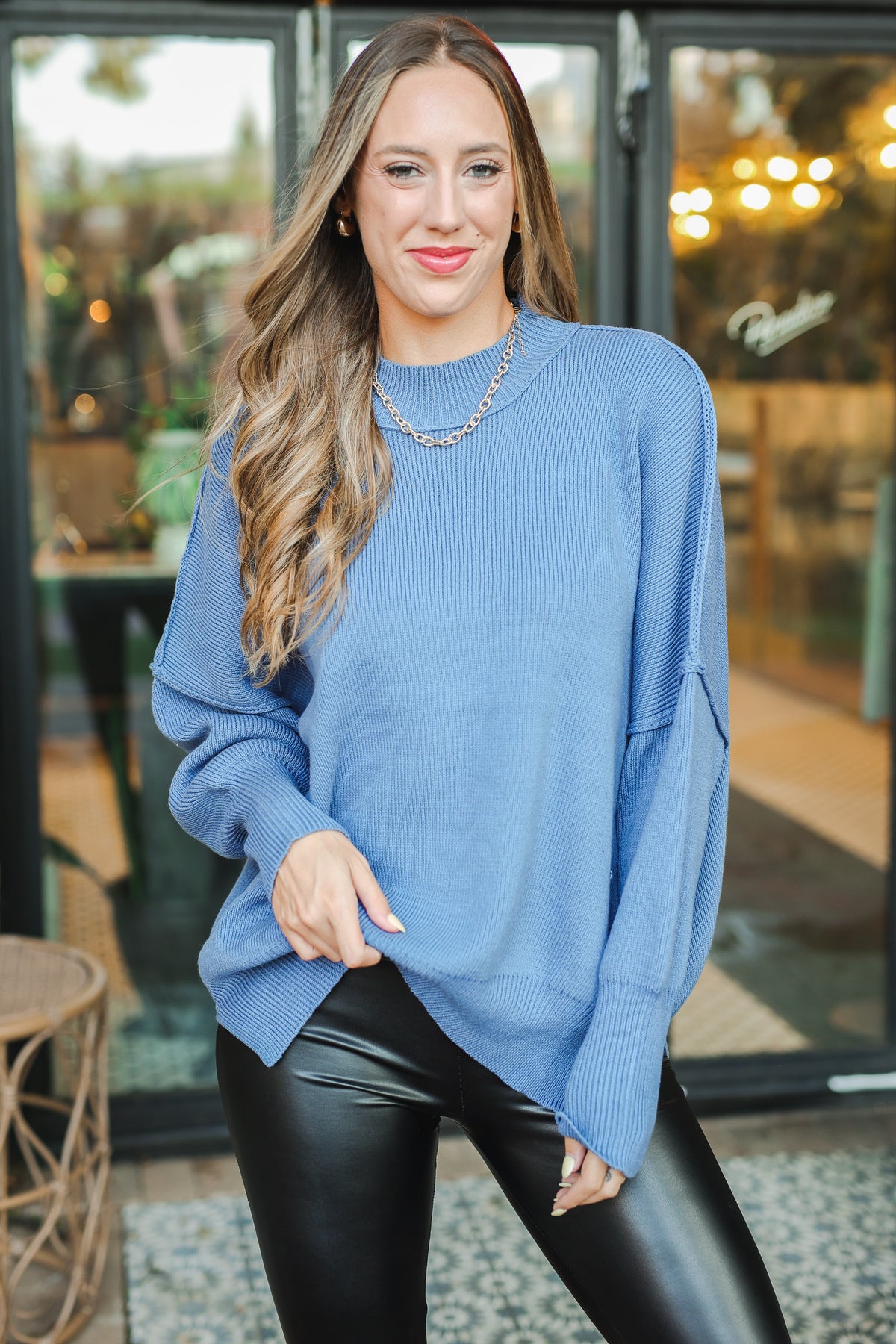 Woman wearing a blue sweater and black leather pants in an outdoor setting.
