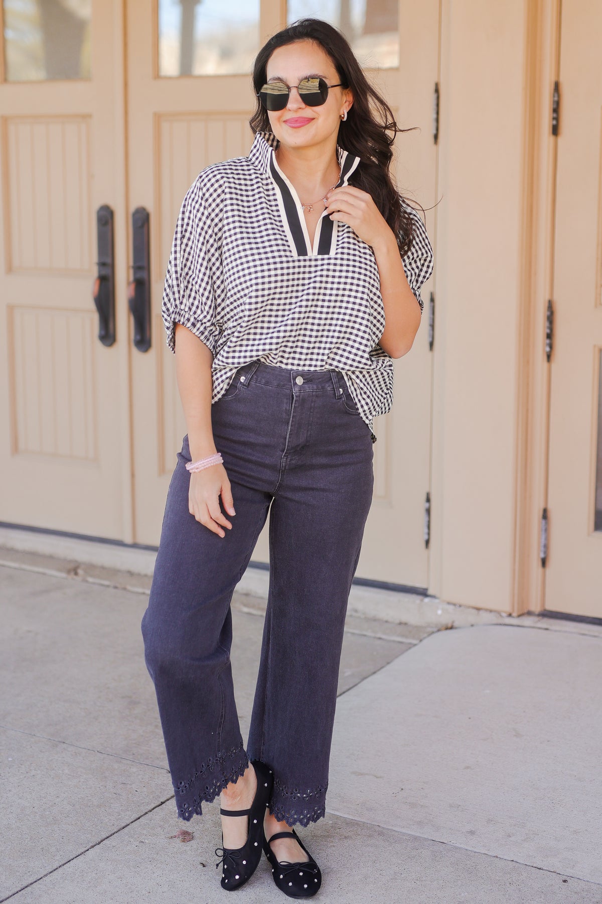 Woman wearing a checkered blouse, dark jeans, and sunglasses outdoors.