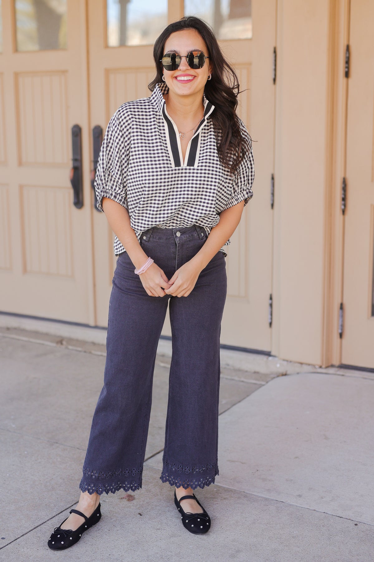 Woman wearing a checkered blouse and dark jeans standing in front of a beige door.