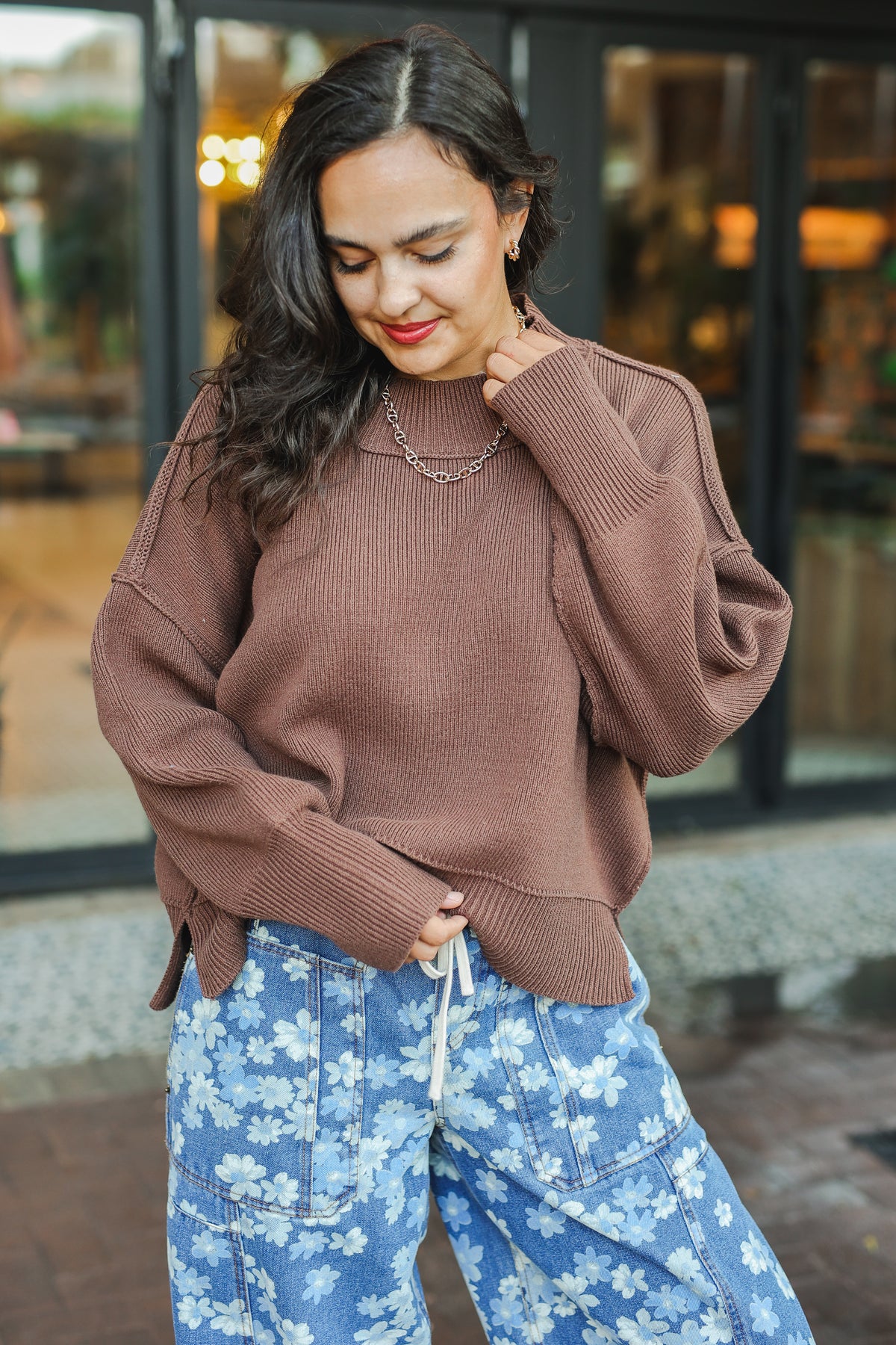 Woman wearing a brown sweater and blue floral pants outdoors.