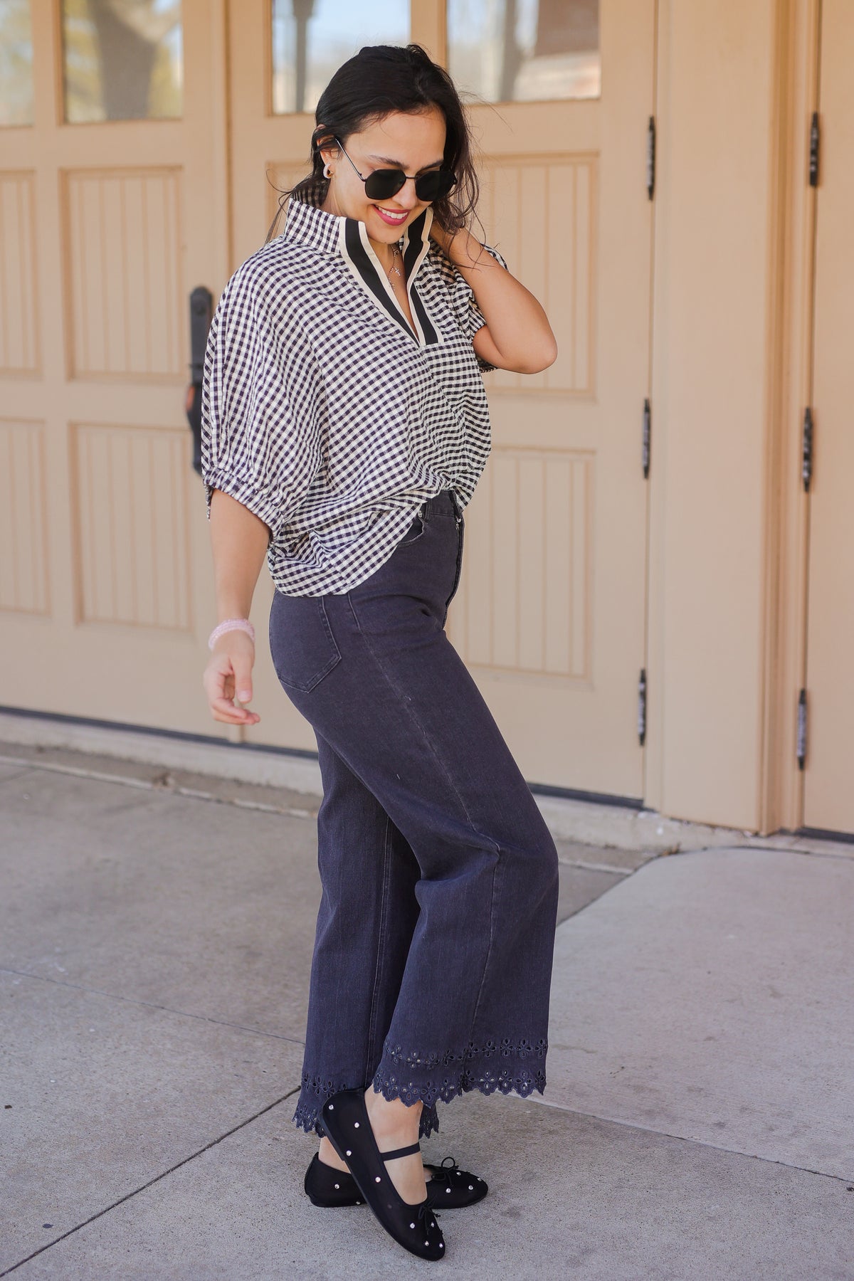 Woman wearing a checkered blouse and dark pants standing in front of a beige door.